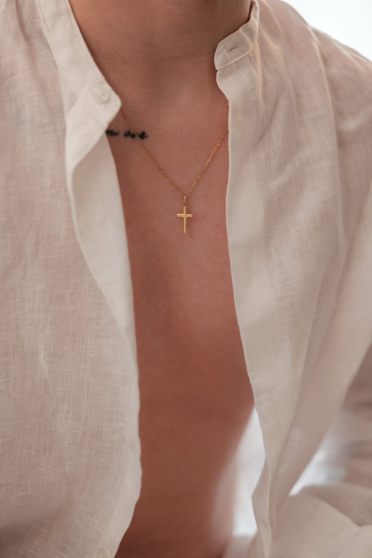 Gros plan sur le buste de William, chemise en lin ouverte, collier à croix dorée, lumière naturelle douce