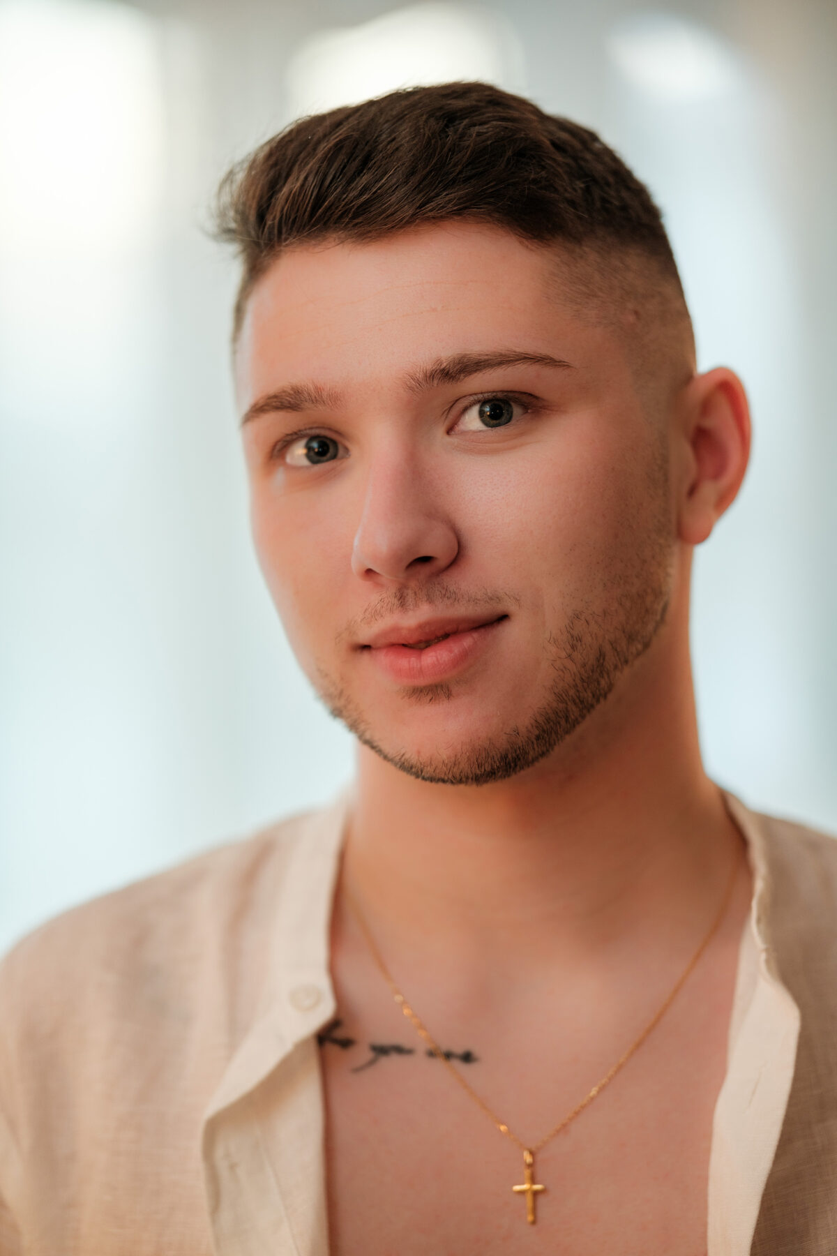 Portrait de William, chemise beige ouverte, collier à croix dorée, lumière naturelle tamisée