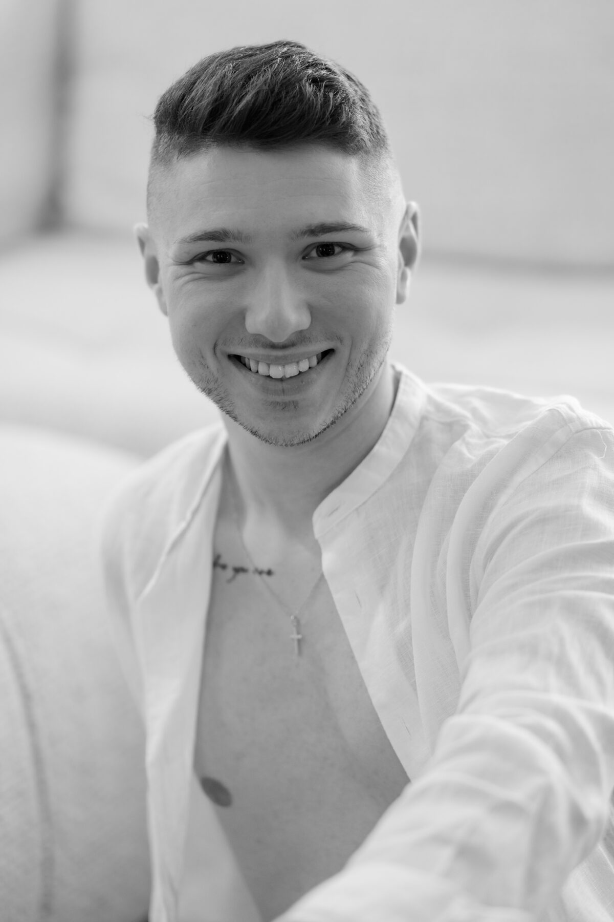 Portrait souriant de William, chemise blanche ouverte, collier à croix, noir et blanc