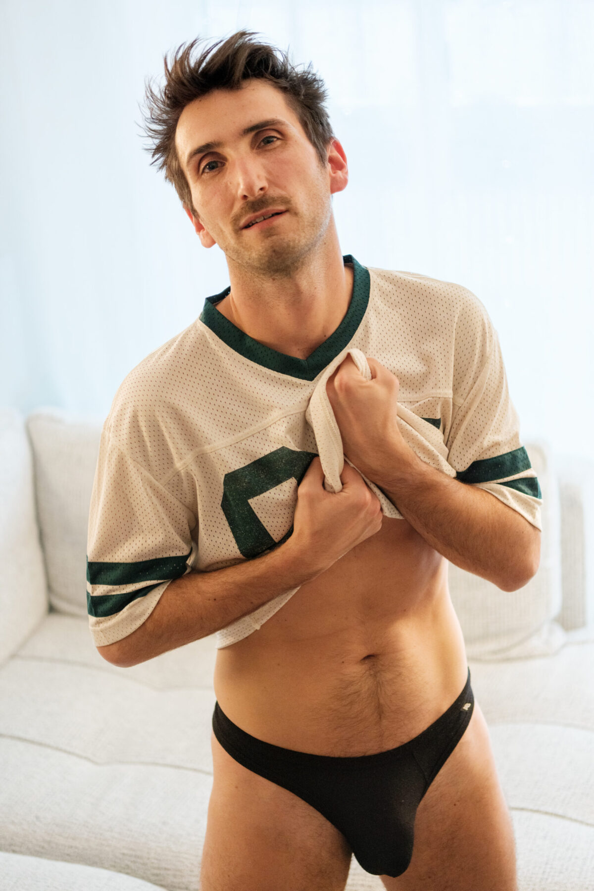 T. soulevant un maillot, torse dévoilé, lumière naturelle — portrait masculin