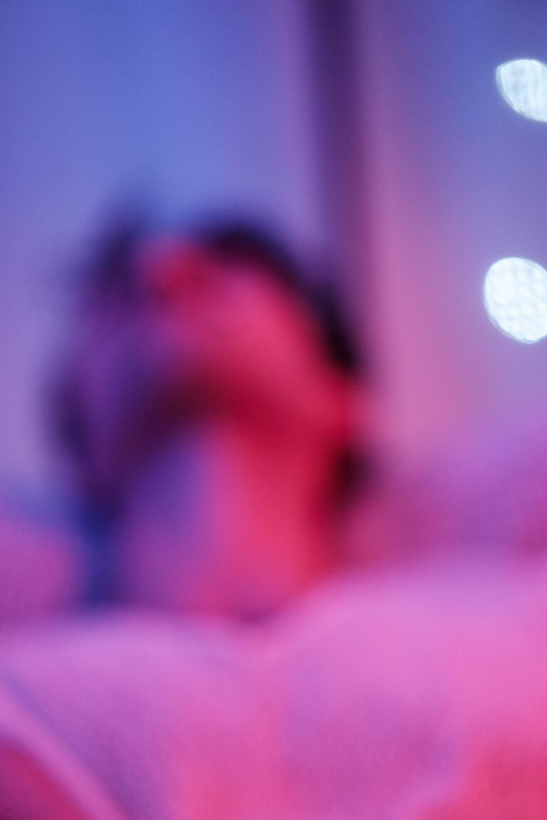 Silhouette floue de T. sur un lit, halos de lumière rose et bleue — photographie d'atmosphère