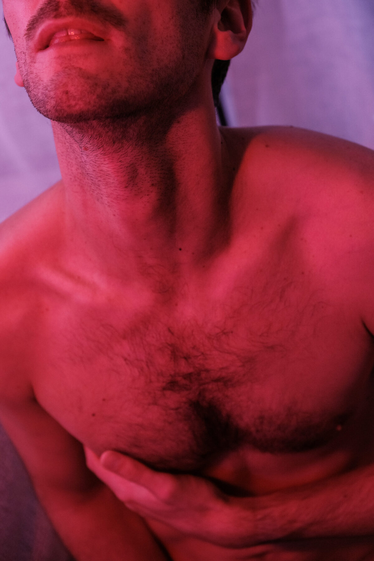 T. menton levé, torse nu, main sur la poitrine, lumière rouge — portrait sensuel