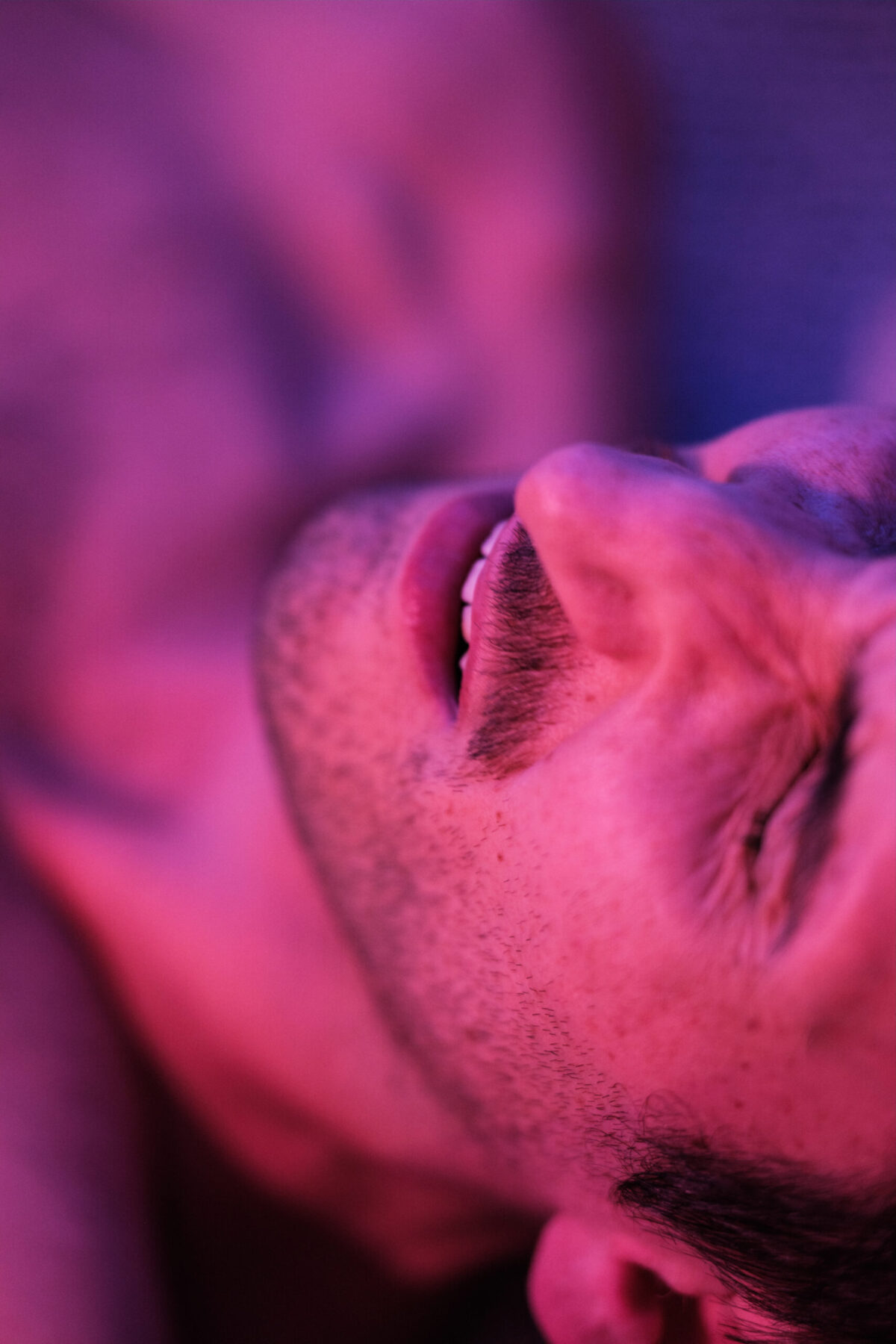 Visage de T. renversé, yeux clos, lumière magenta — portrait sensuel
