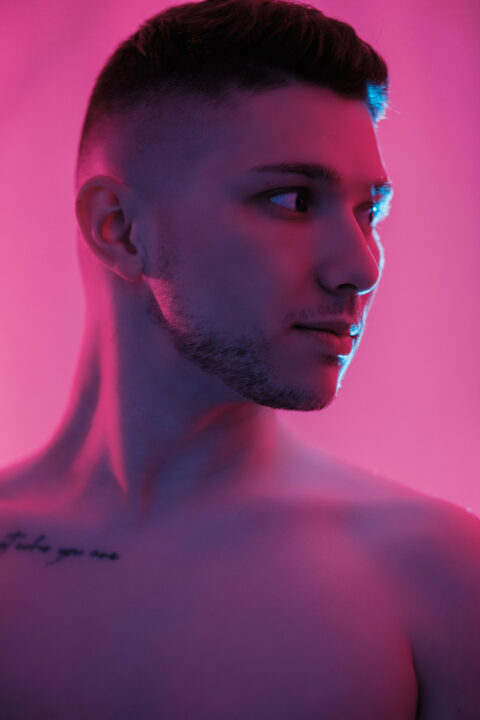 Portrait de William torse nu, éclairage saturé en rose et bleu, regard sur le côté