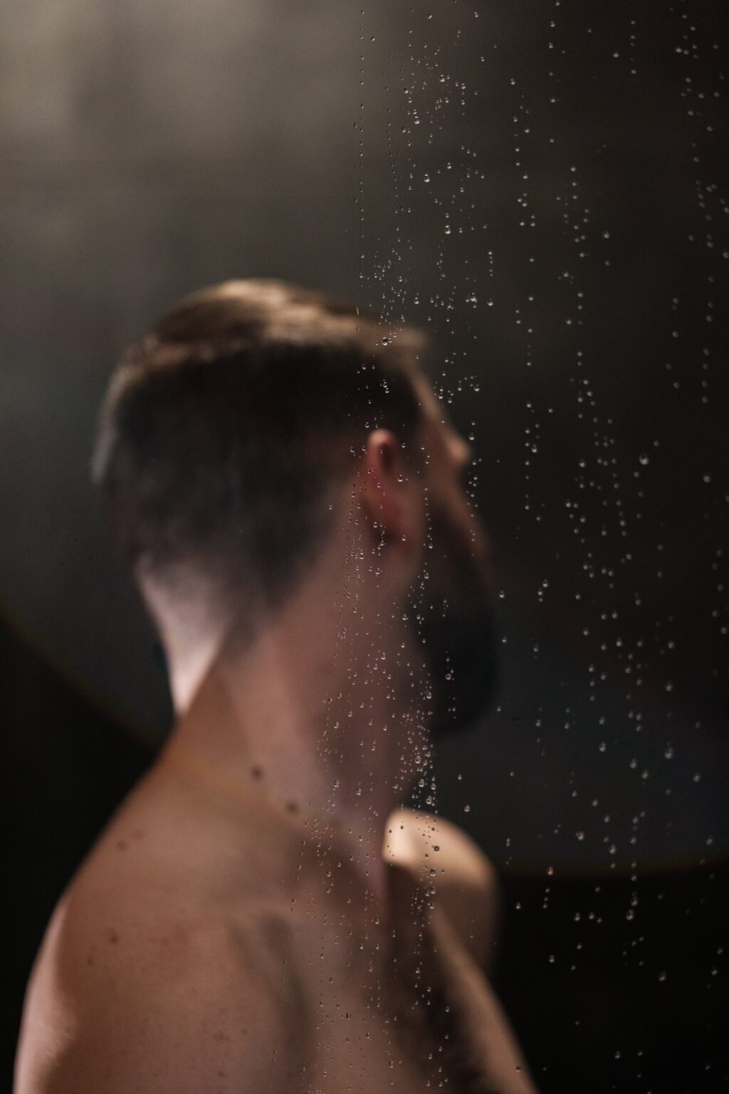François de dos derrière une vitre de gouttes, regard par-dessus l'épaule — nu artistique