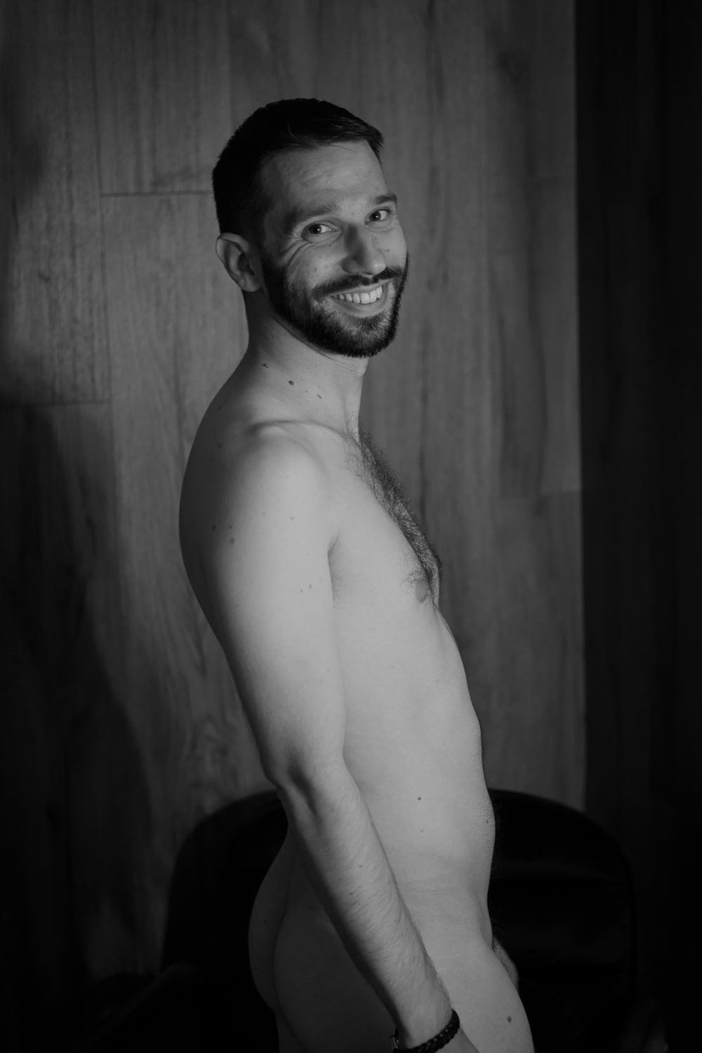 François nu de profil, sourire, fond bois — nu artistique masculin noir et blanc