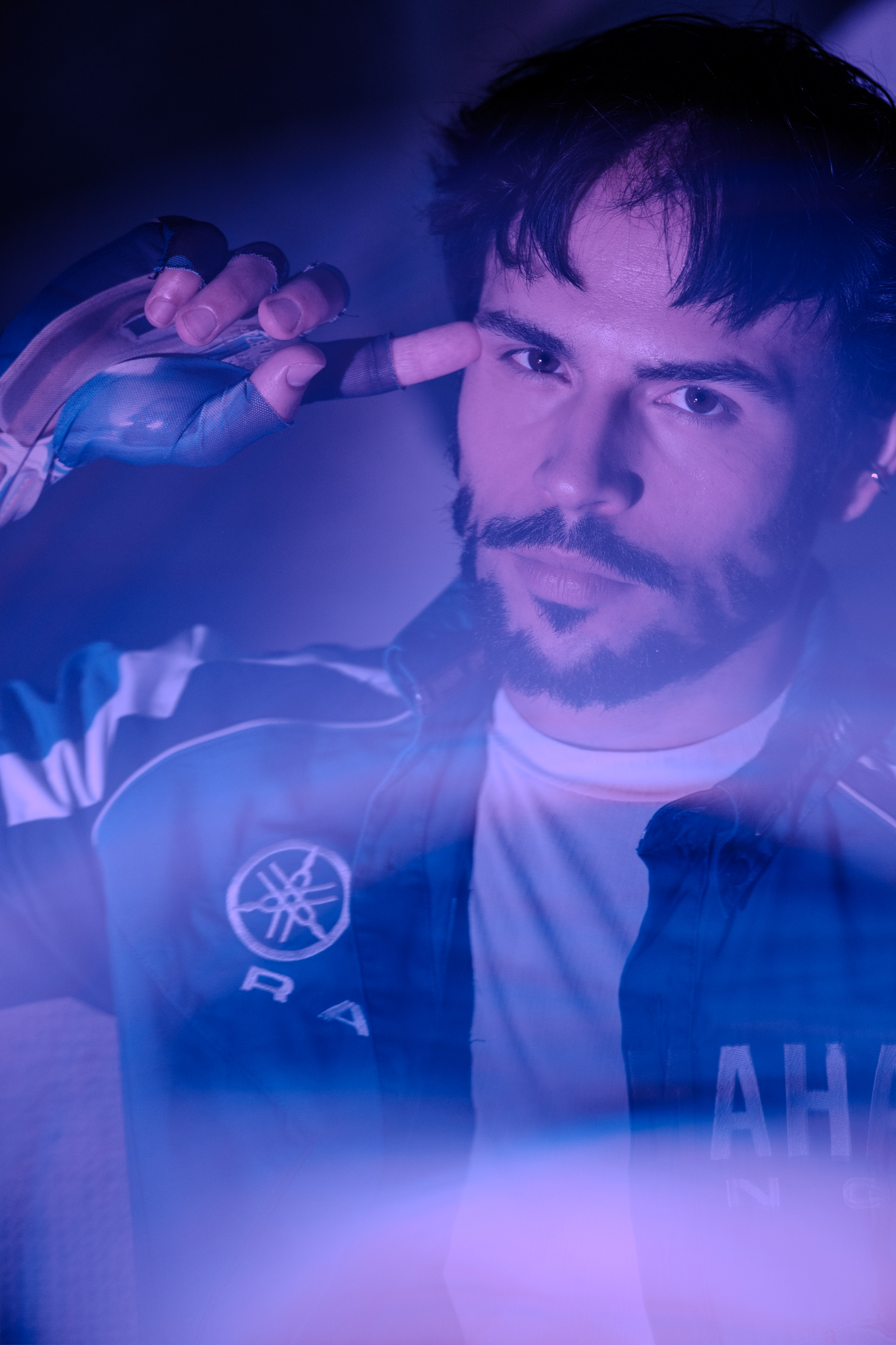 Portrait d'Hugo en blouson de course Yamaha Racing, lumière bleu-violet néon et regard intense