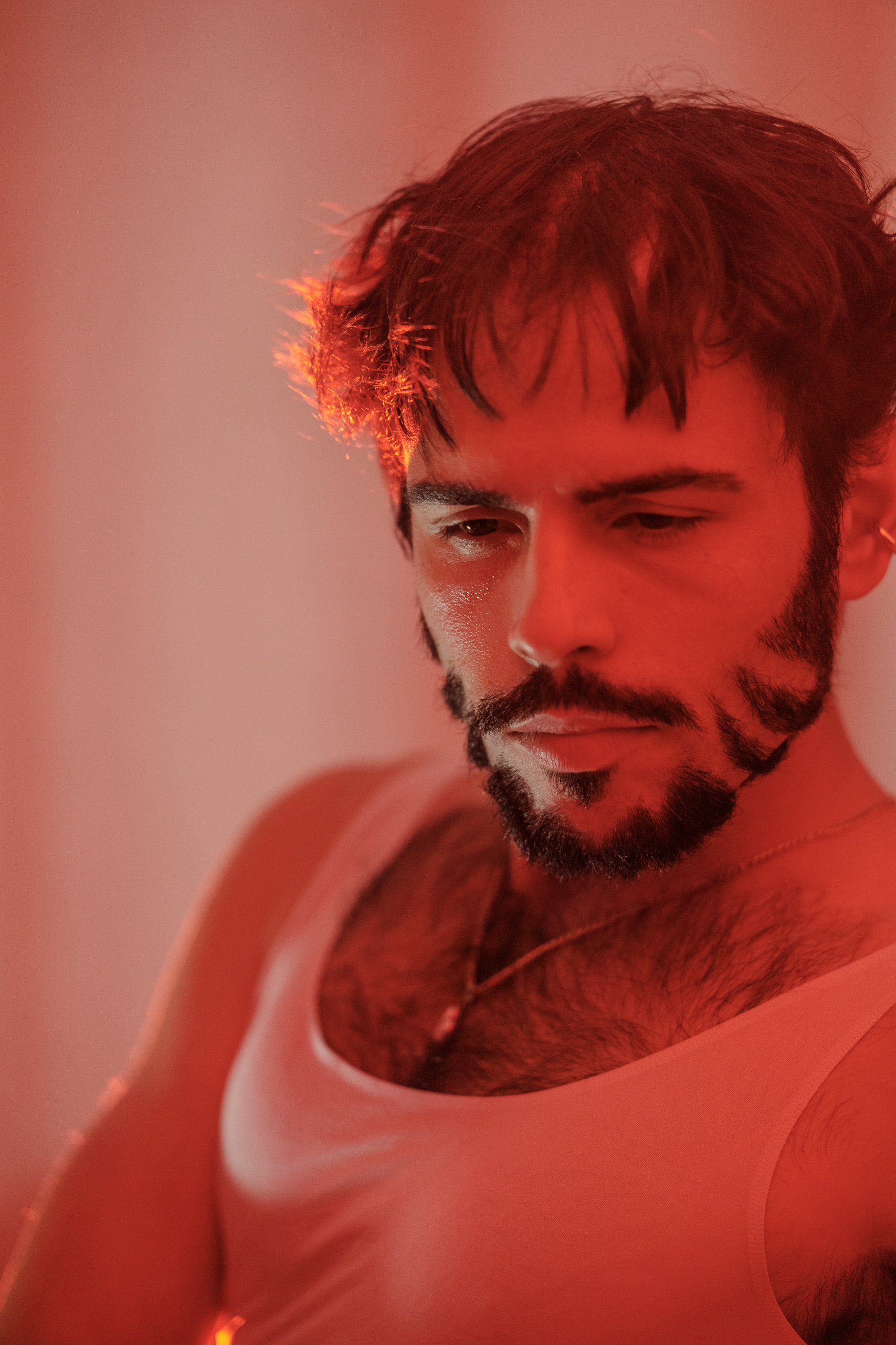 Portrait d'Hugo au regard baissé en débardeur blanc, lumière rouge tamisée