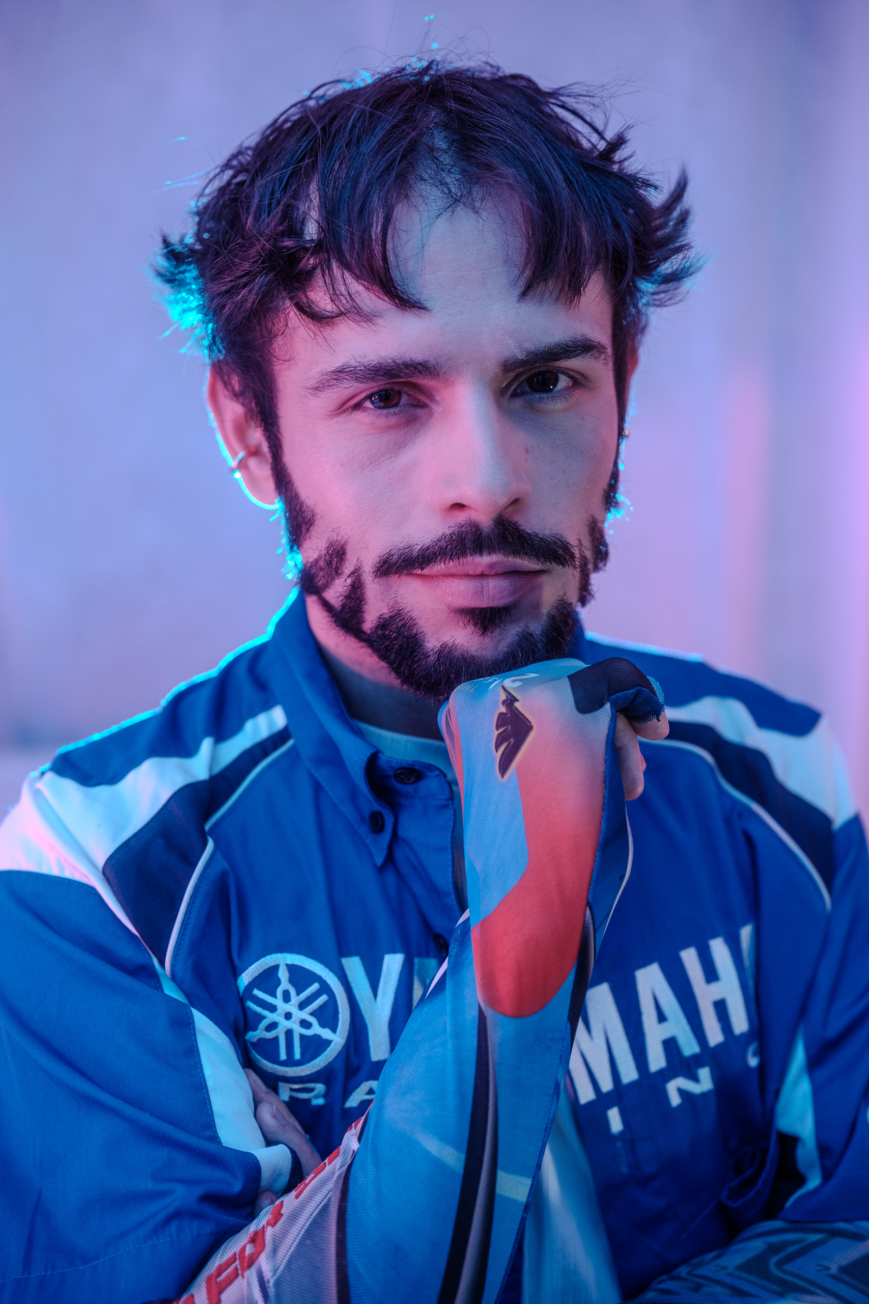 Portrait rapproché d'Hugo en veste Yamaha Racing, éclairage bleu et rose sur fond studio