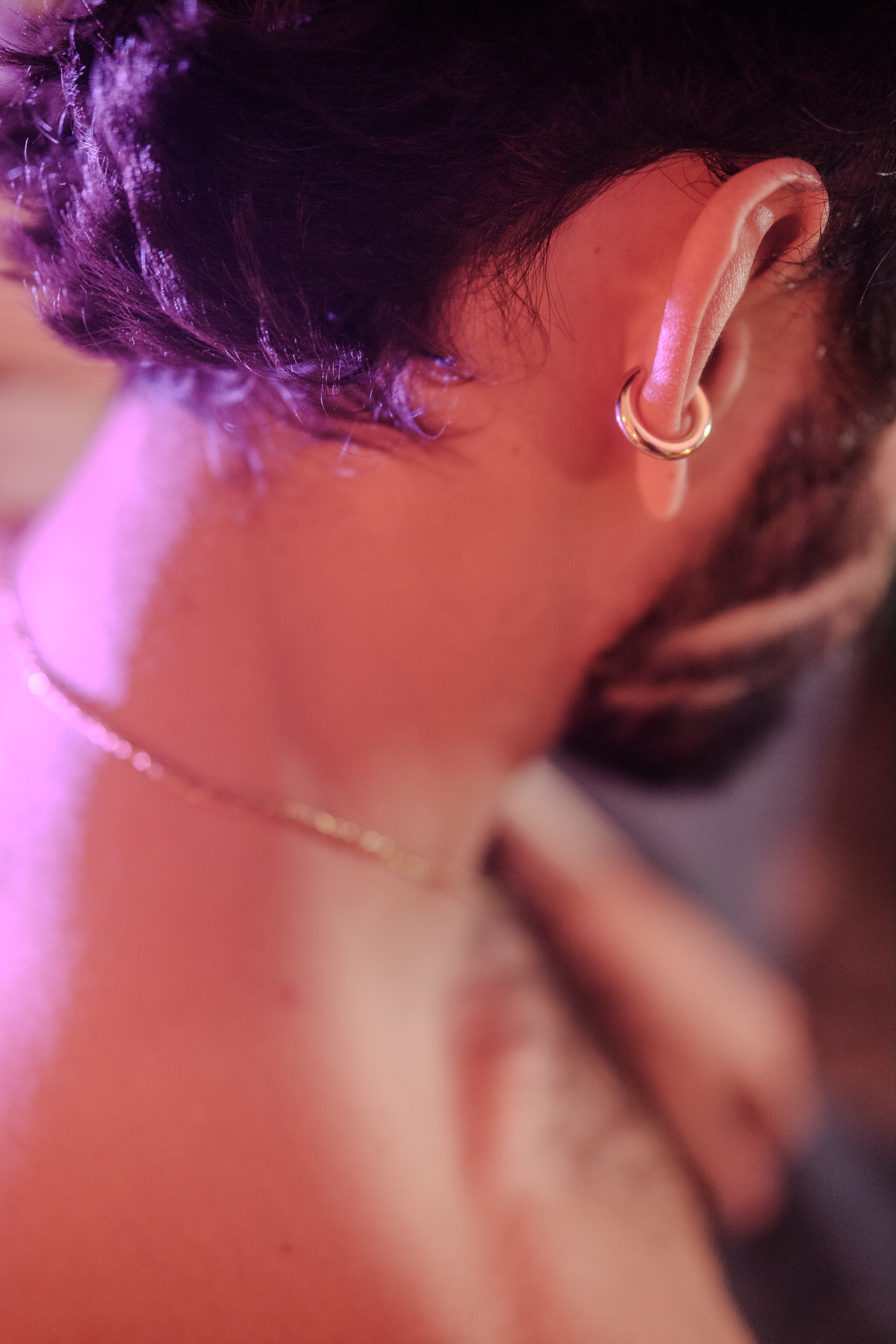 Gros plan sur le cou d'Hugo, bijoux ear cuff et collier, lumière violette et rose