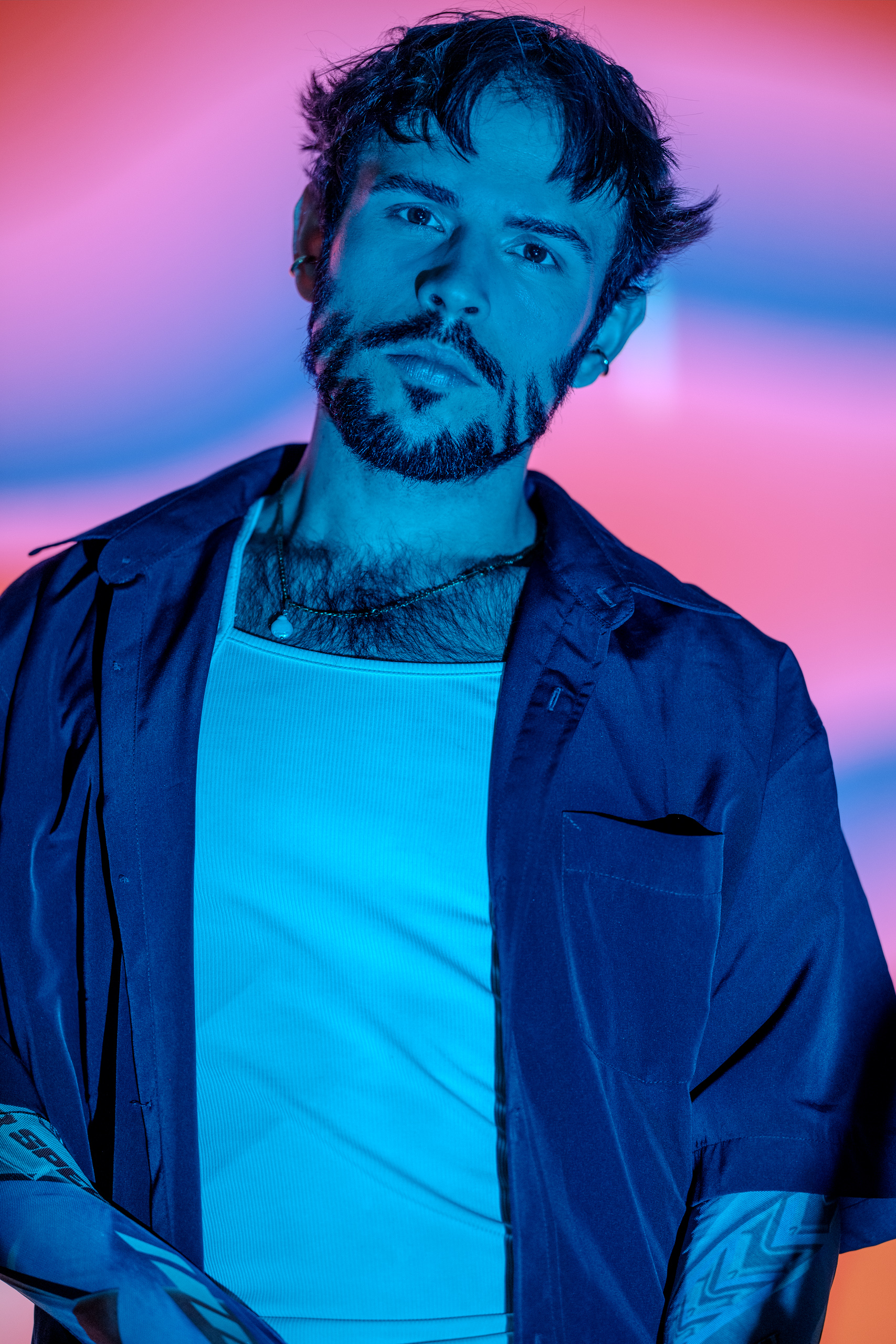 Portrait d'Hugo chemise entrouverte laissant apparaître un tatouage, lumière bleu et rose