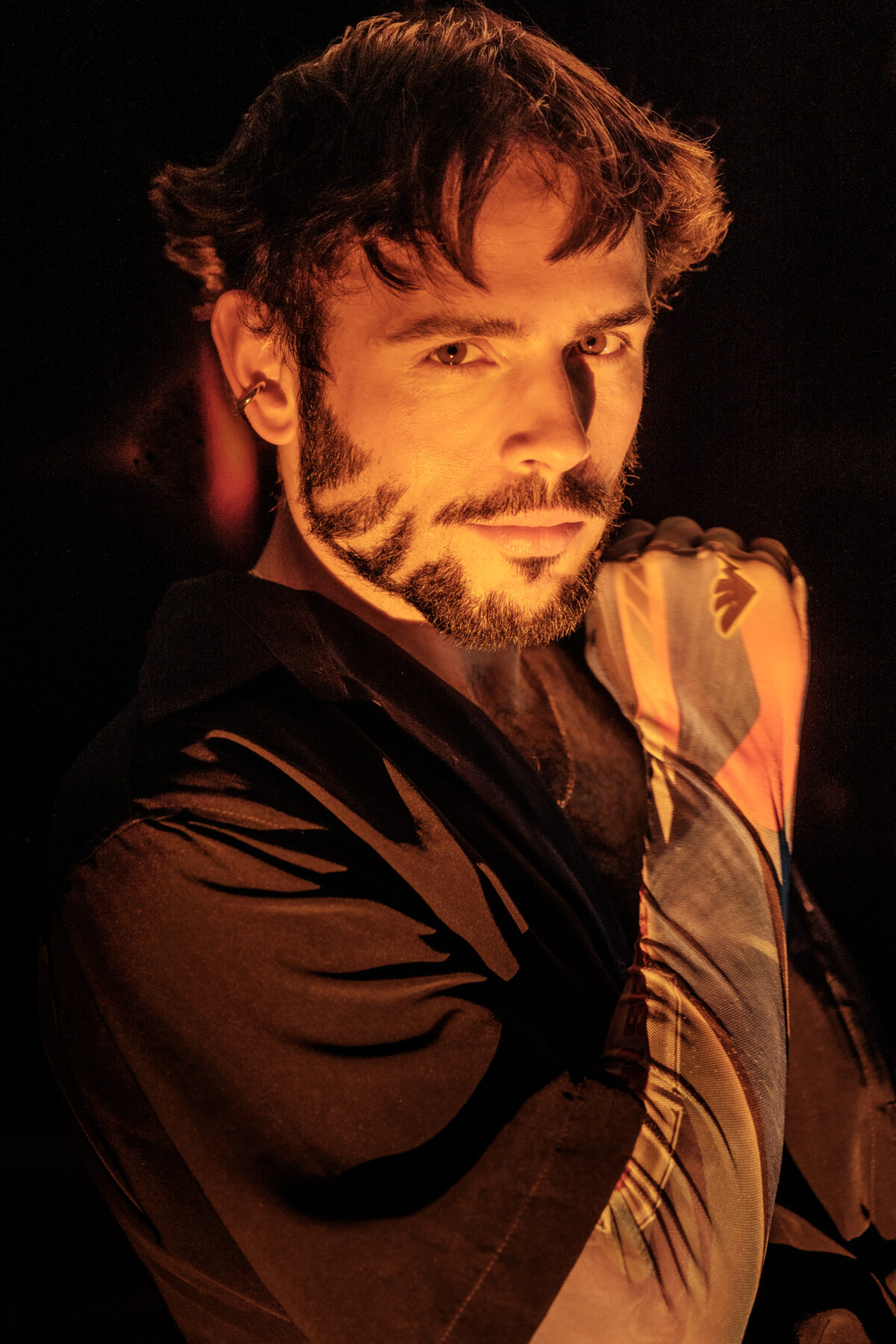 Portrait d'Hugo au regard intense sous une lumière orangée chaude, chemise imprimée