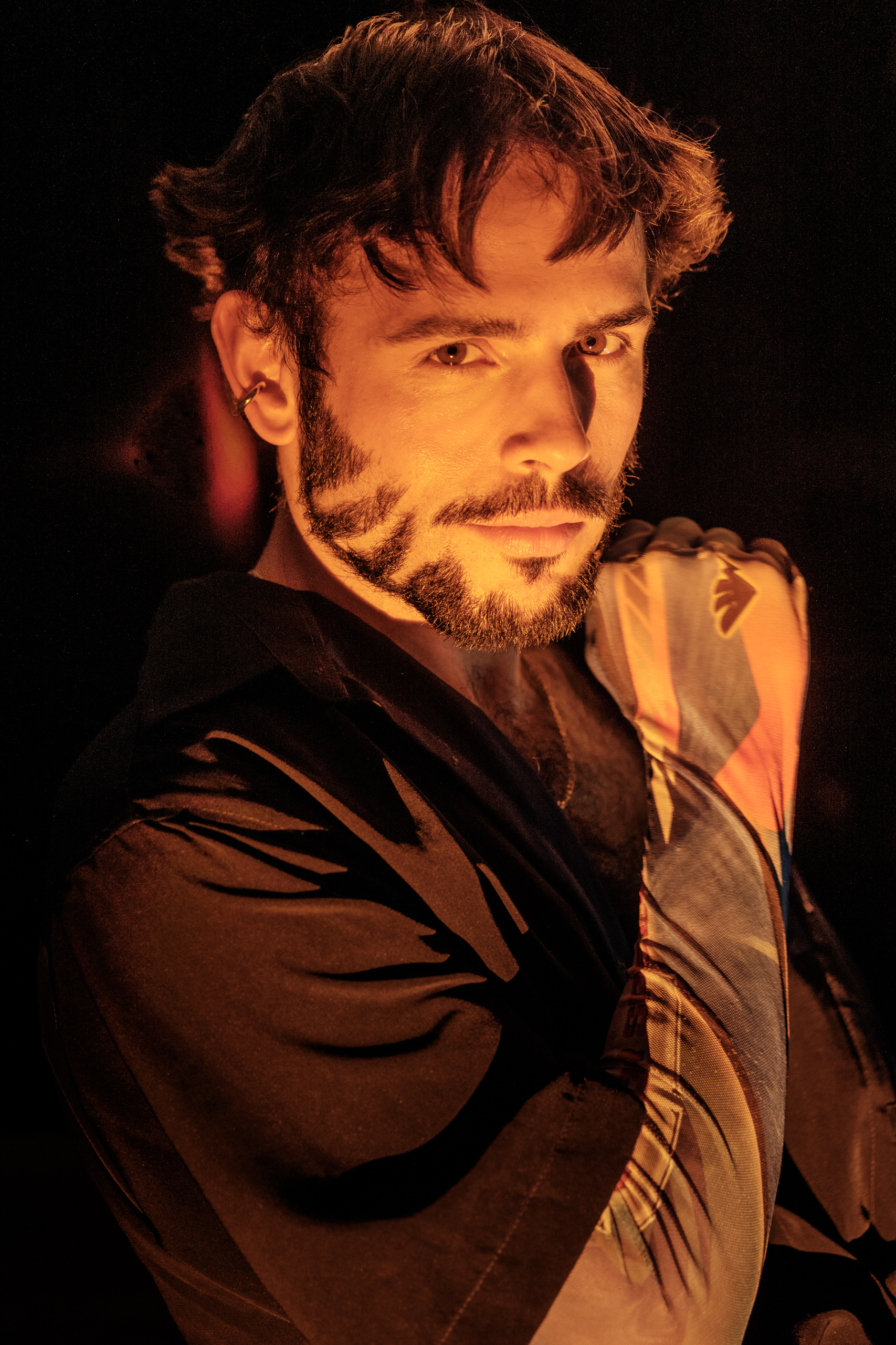 Portrait d'Hugo au regard intense sous une lumière orangée chaude, chemise imprimée