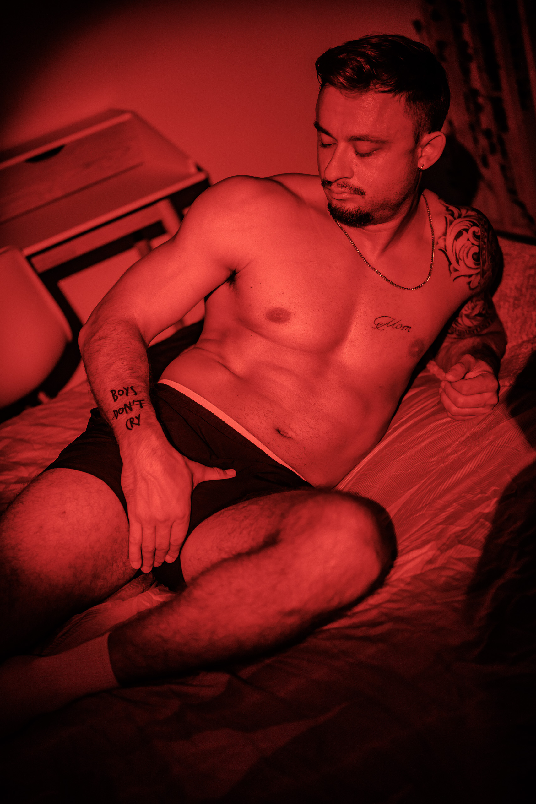 Portrait de KevinHungXL allongé sur un lit, torse nu et short de sport noir, éclairage rouge