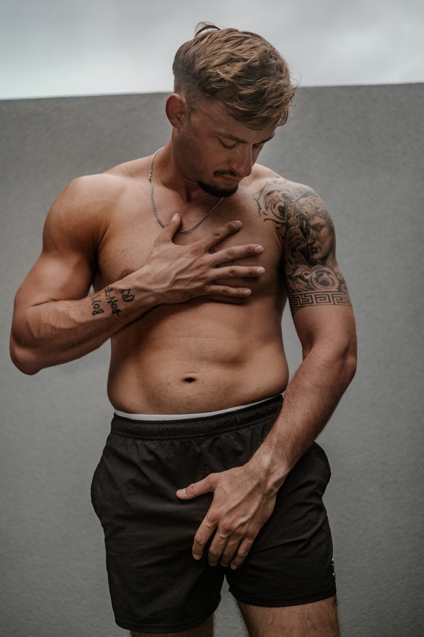 Portrait de KevinHungXL torse nu en extérieur, la main posée sur le torse athlétique