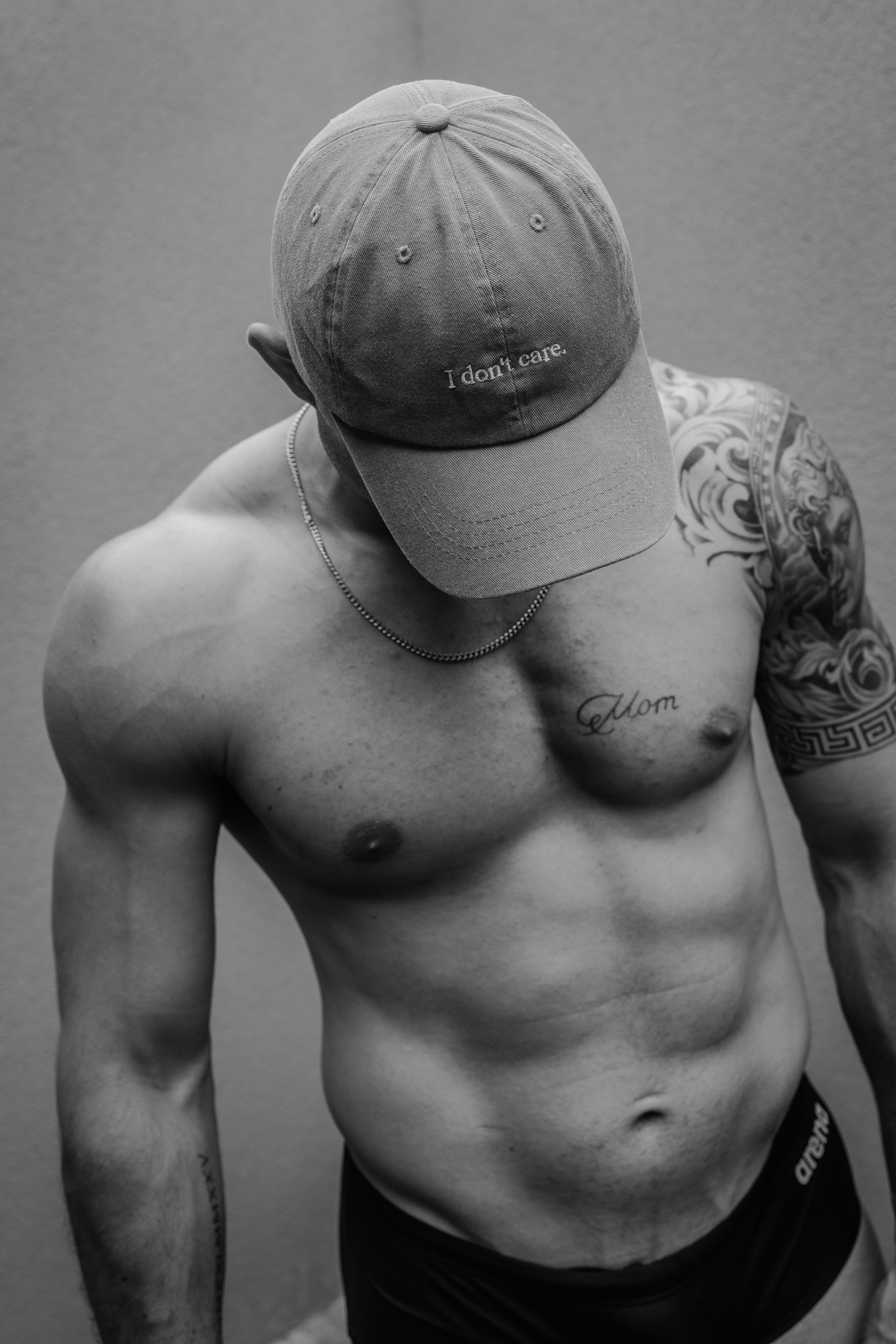Pose en noir et blanc de KevinHungXL, musclé en maillot de bain, visage caché par une casquette avec inscription "I don't care"