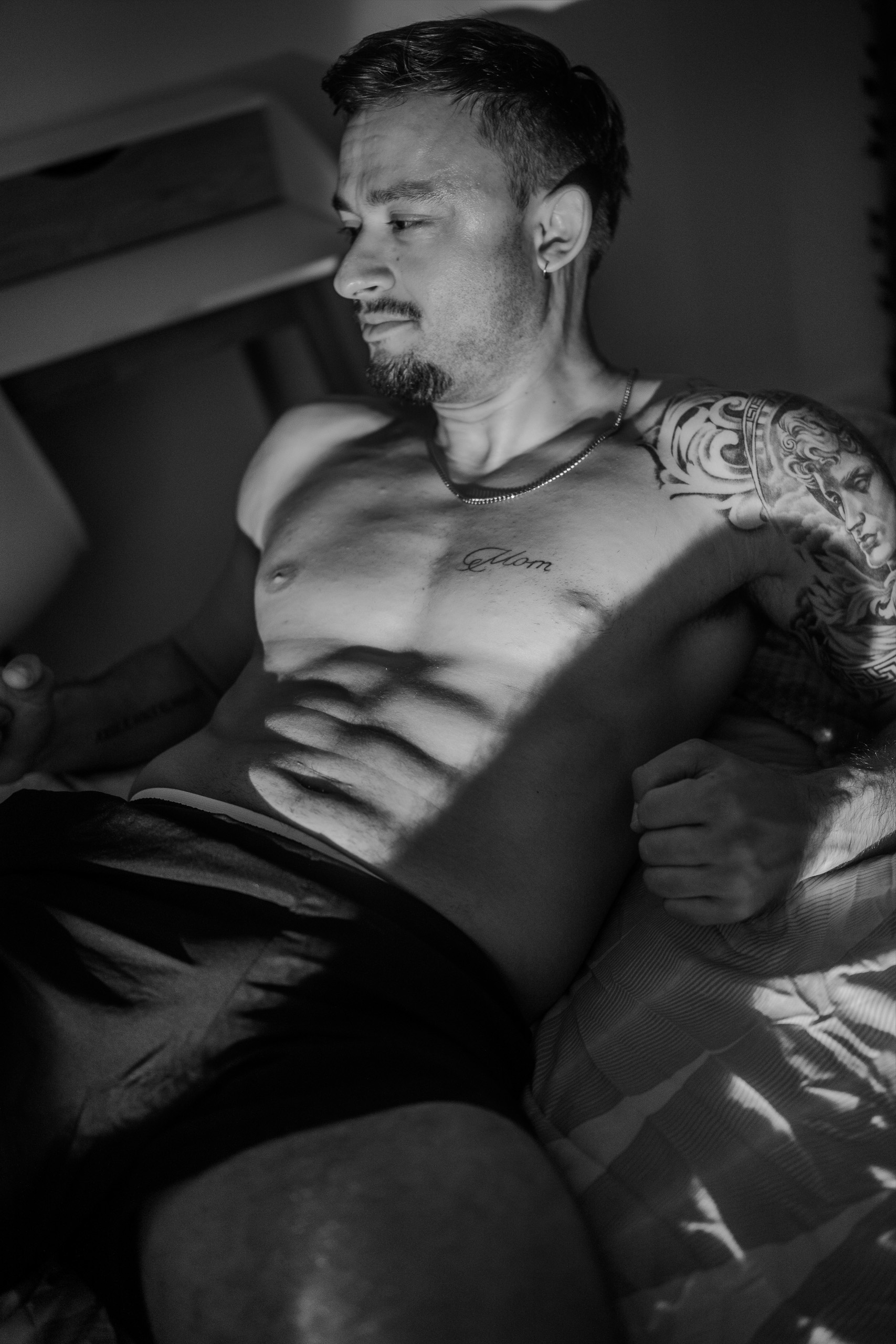 Portrait de KevinHungXL torse nu, allongé sur un lit, photo en noir et blanc