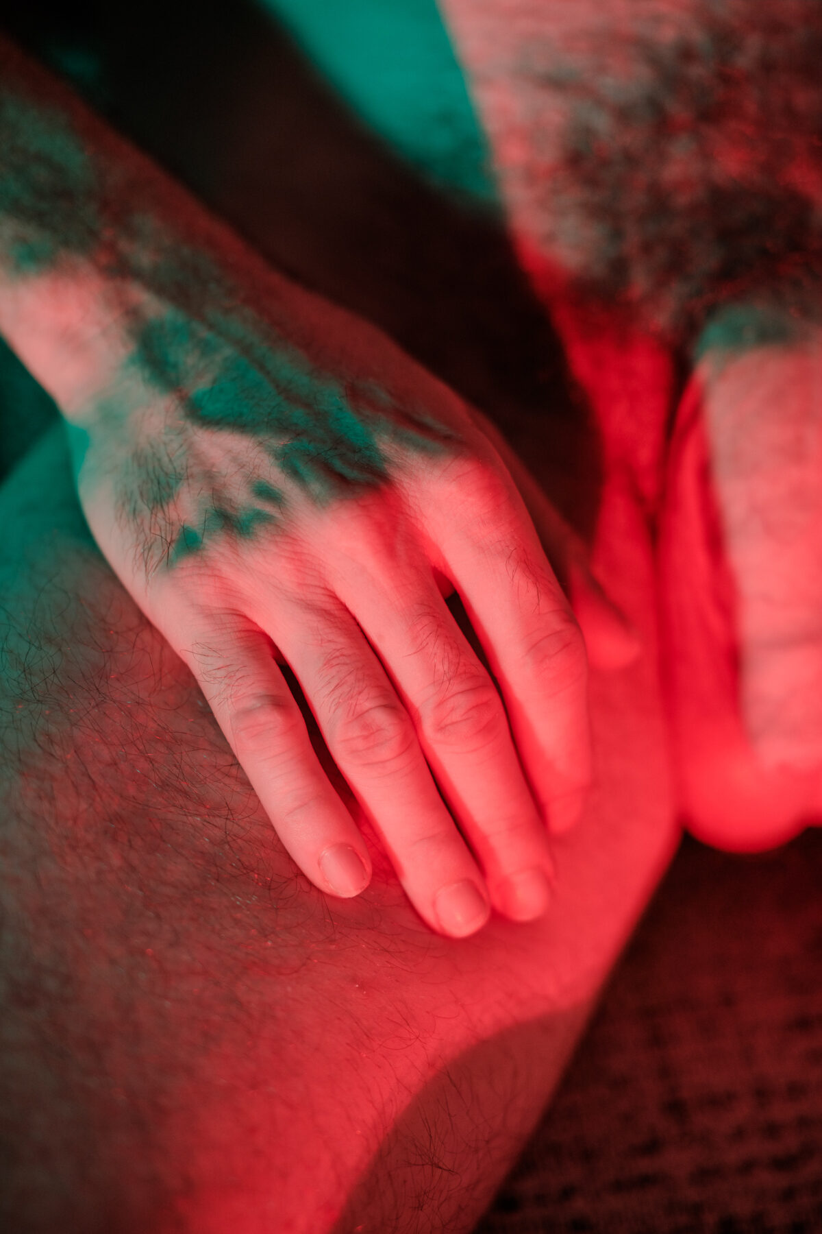 Nahaufnahme einer Hand, die auf Clements Oberschenkel ruht, in rotem und grünem Licht.