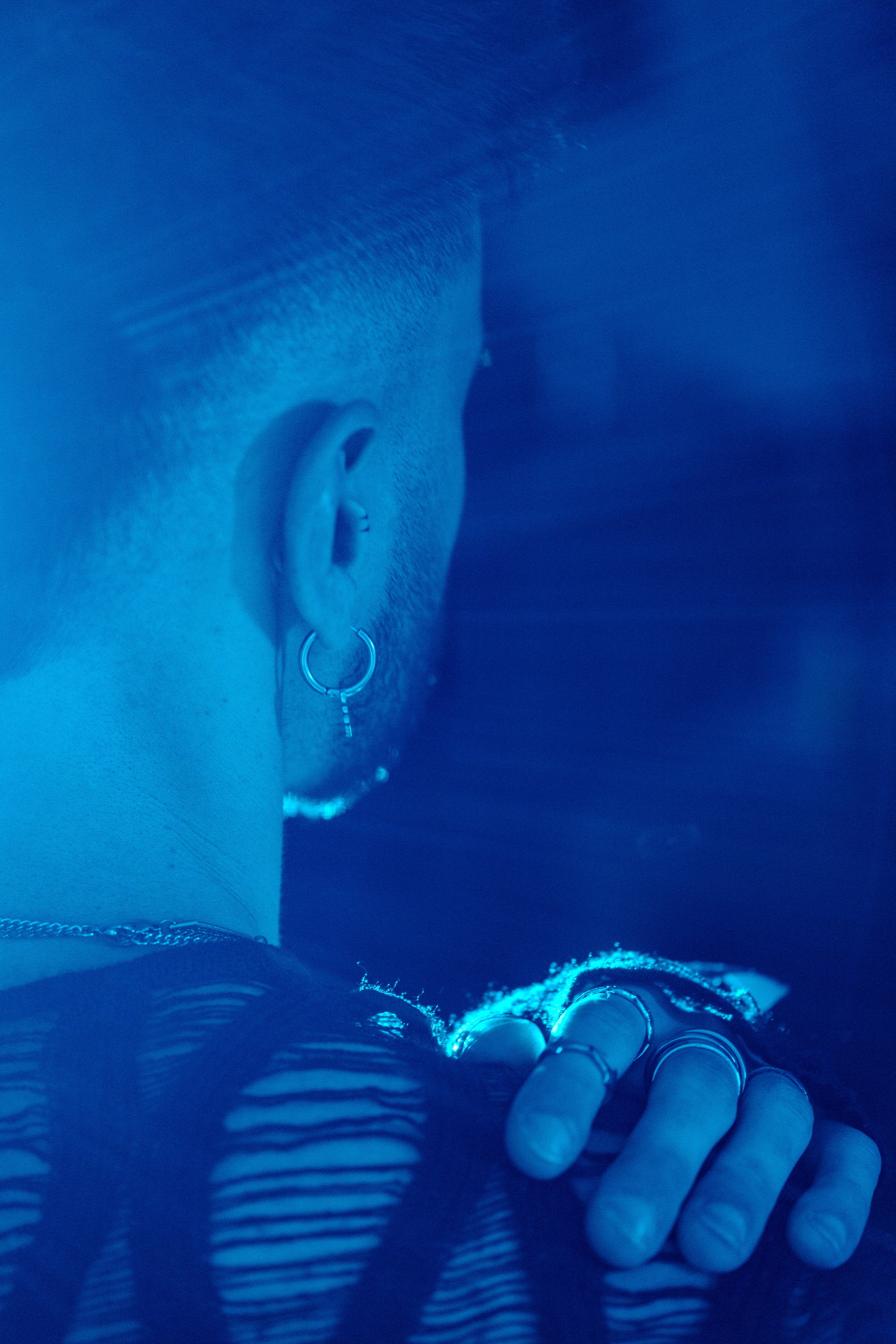 Gros plan sur une oreille percée et une main baguée, éclairage bleu nuit.