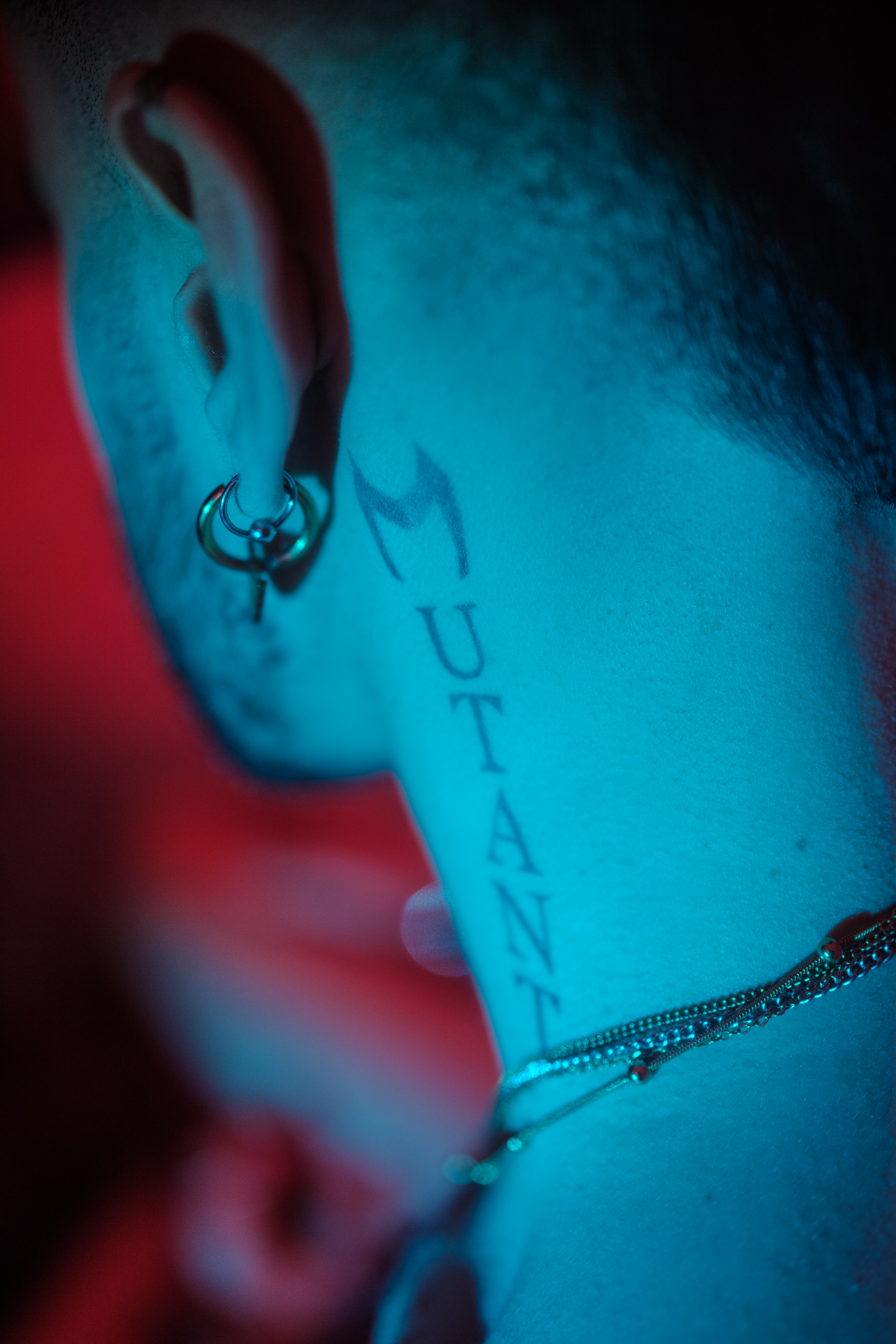 Gros plan sur un tatouage au cou et une boucle d'oreille, éclairage bleu.