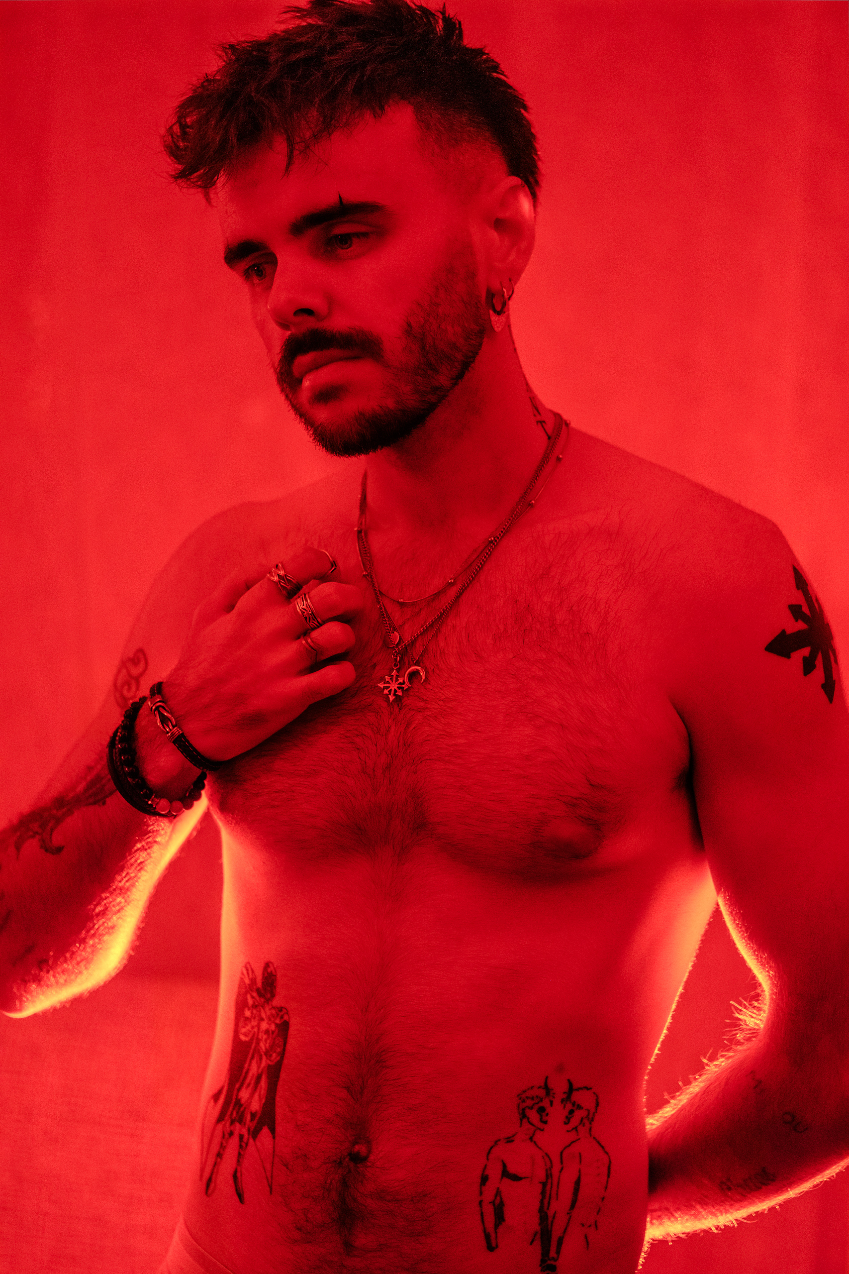 Portrait torse nu, bagues et bracelets, tatouages, éclairage rouge.