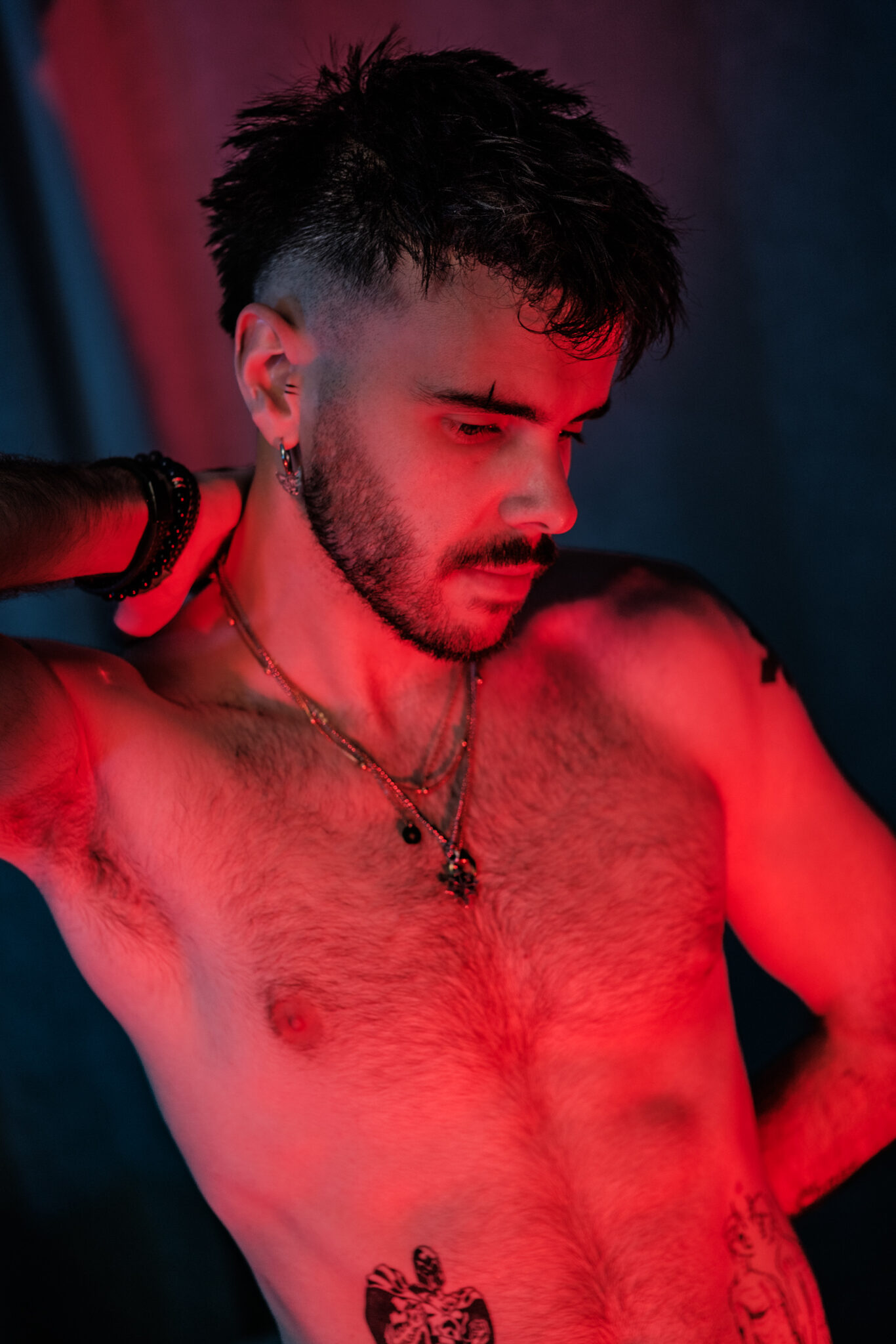 Portrait torse nu, tatouages et colliers, éclairage rouge et bleu.