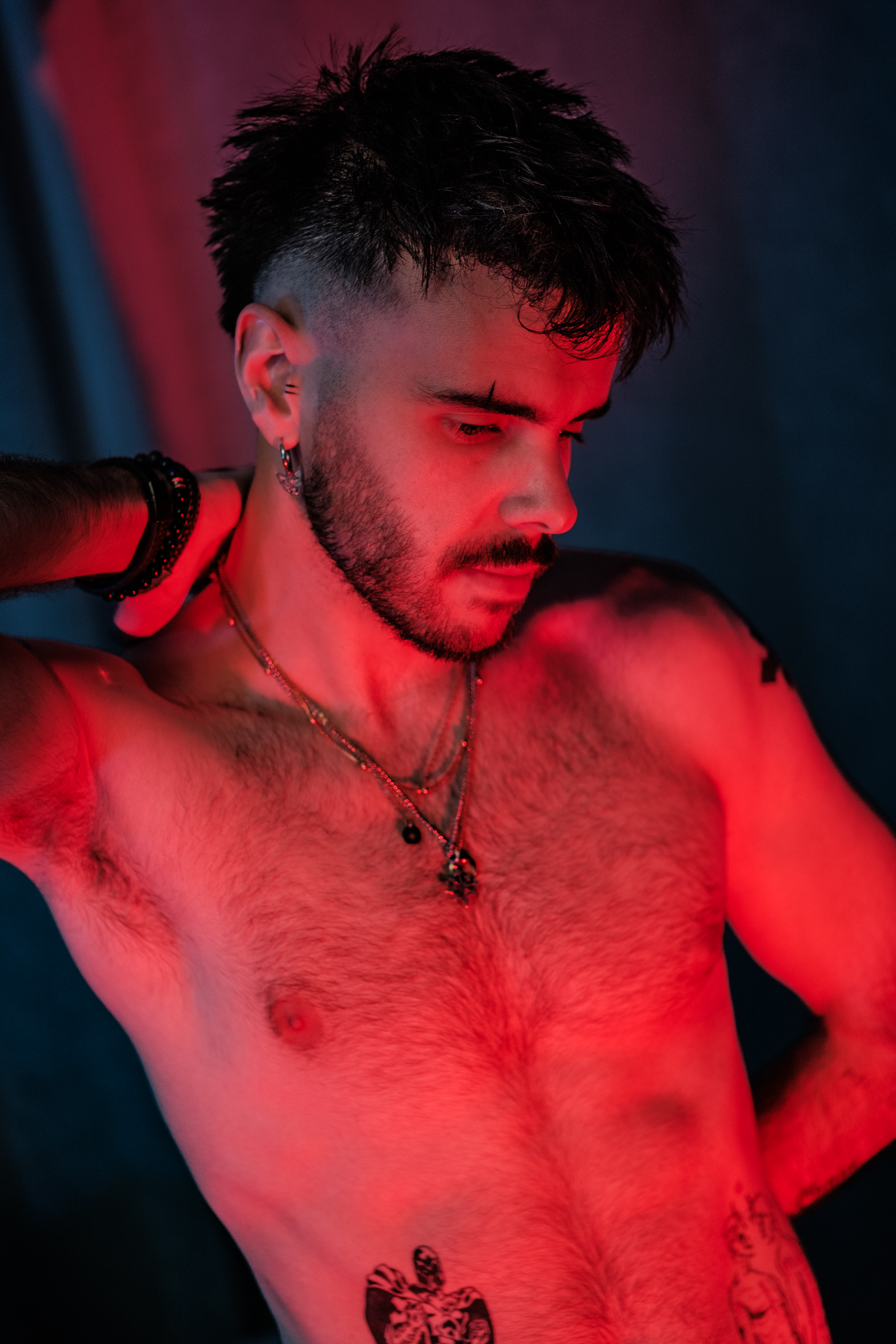 Portrait torse nu, tatouages et colliers, éclairage rouge et bleu.