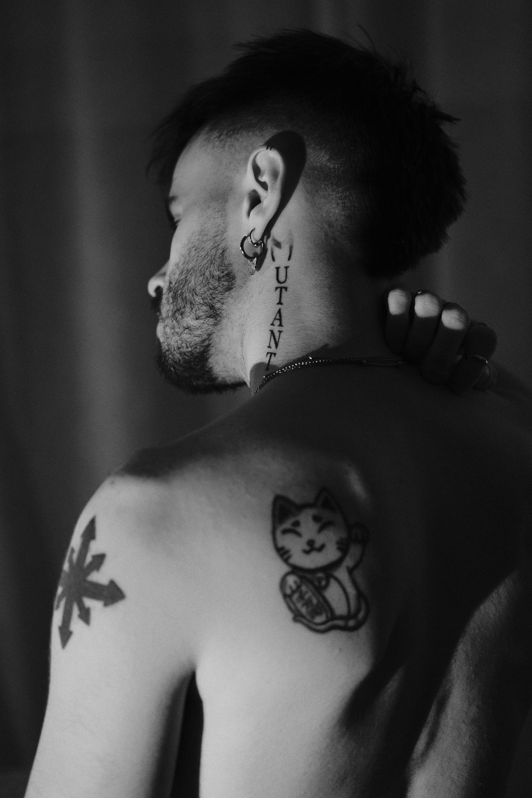 Portrait de dos en noir et blanc, tatouages à l'épaule et au cou.