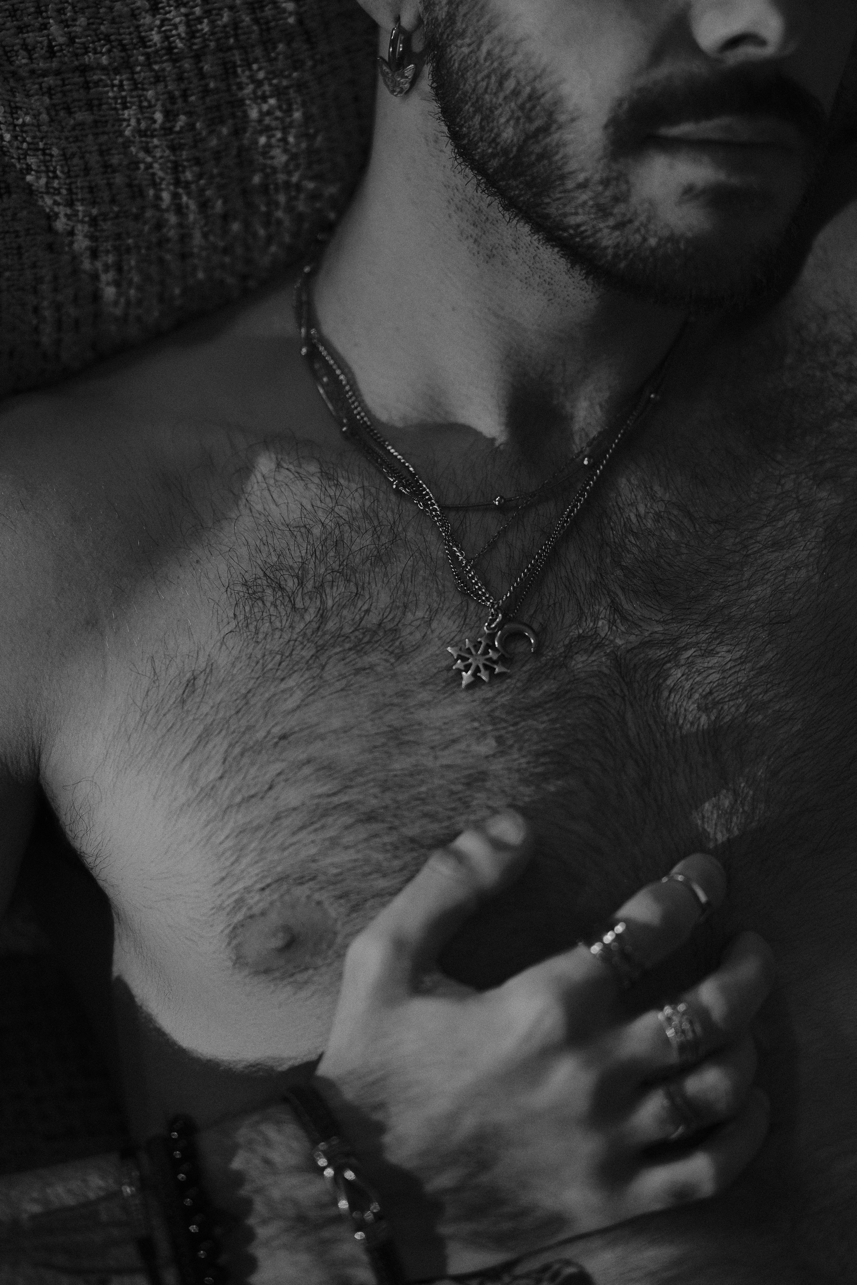 Gros plan sur le torse et colliers, main baguée, noir et blanc.