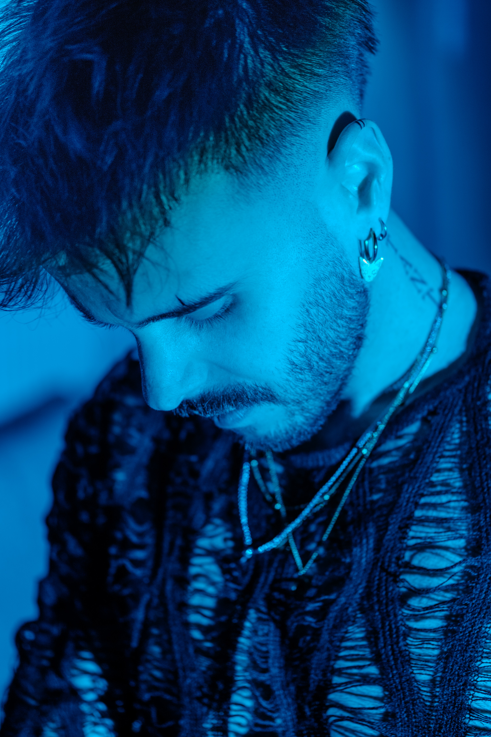 Portrait rapproché, colliers et tatouage au cou, éclairage bleu.