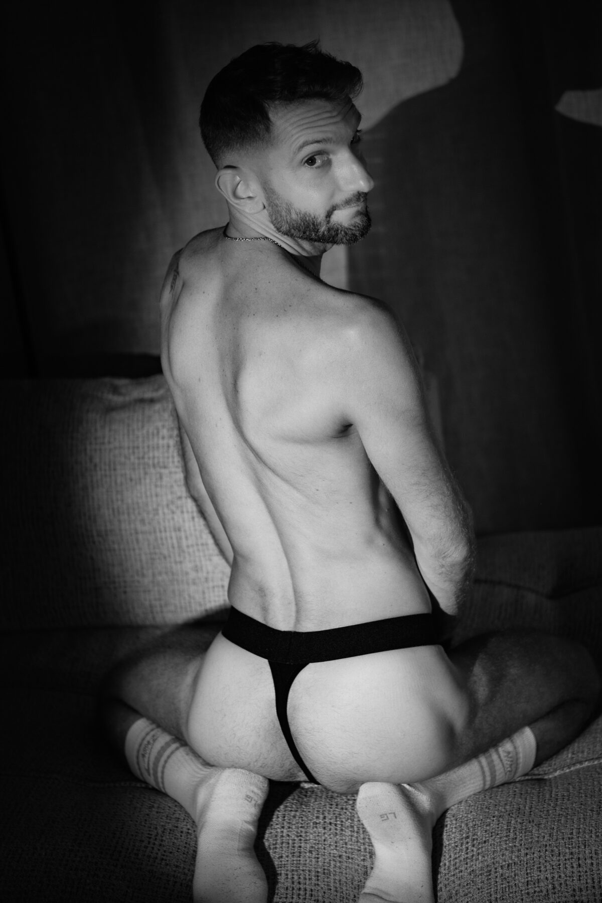 Loukas More de dos en jockstrap noir, noir et blanc, photographie artistique masculine sur canapé.