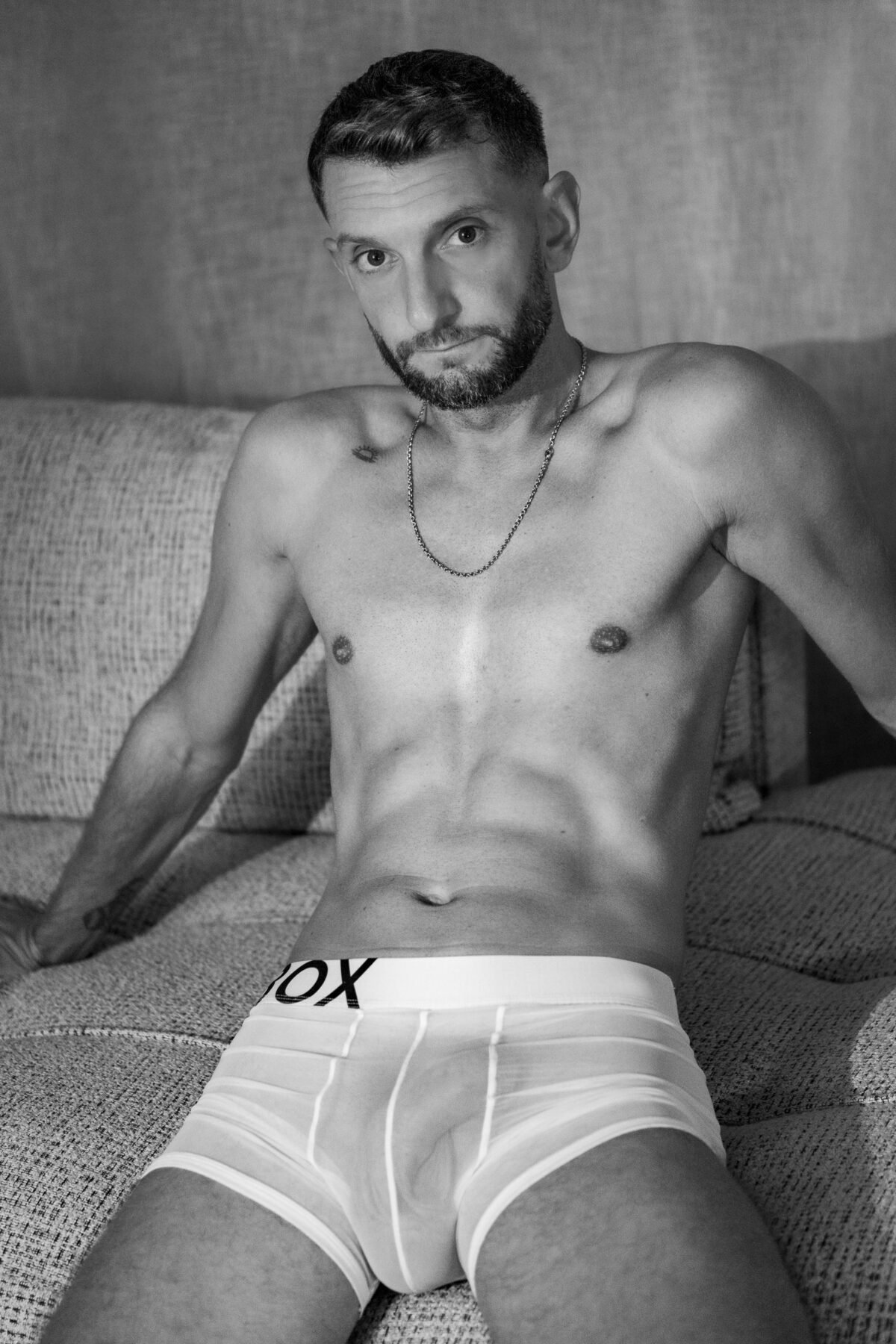 Portrait de Loukas More assis en boxer blanc, regard caméra, photographie de mode masculine.
