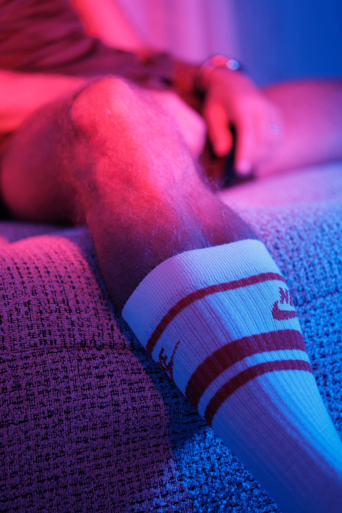 Loukas More, gros plan sur la jambe et la chaussette, ambiance néon rose et bleu, photographie artistique masculine.