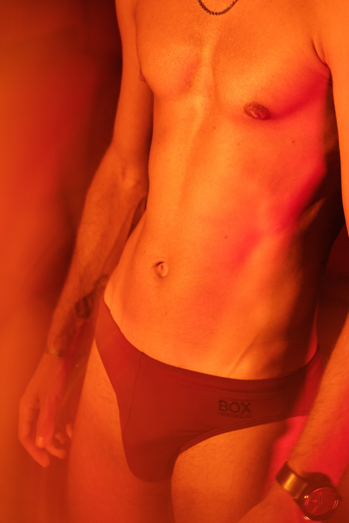 Loukas More en sous-vêtement bordeaux, tons orange chauds, photographie de mode masculine sensuelle.