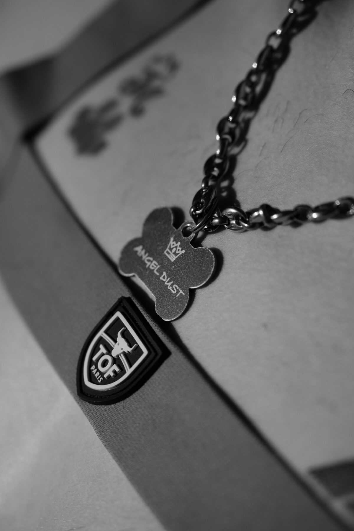 Macro noir et blanc sur la médaille "Angel Dust" en forme d'os et l'écusson "TOF Paris" du harnais, chaîne en gros plan.