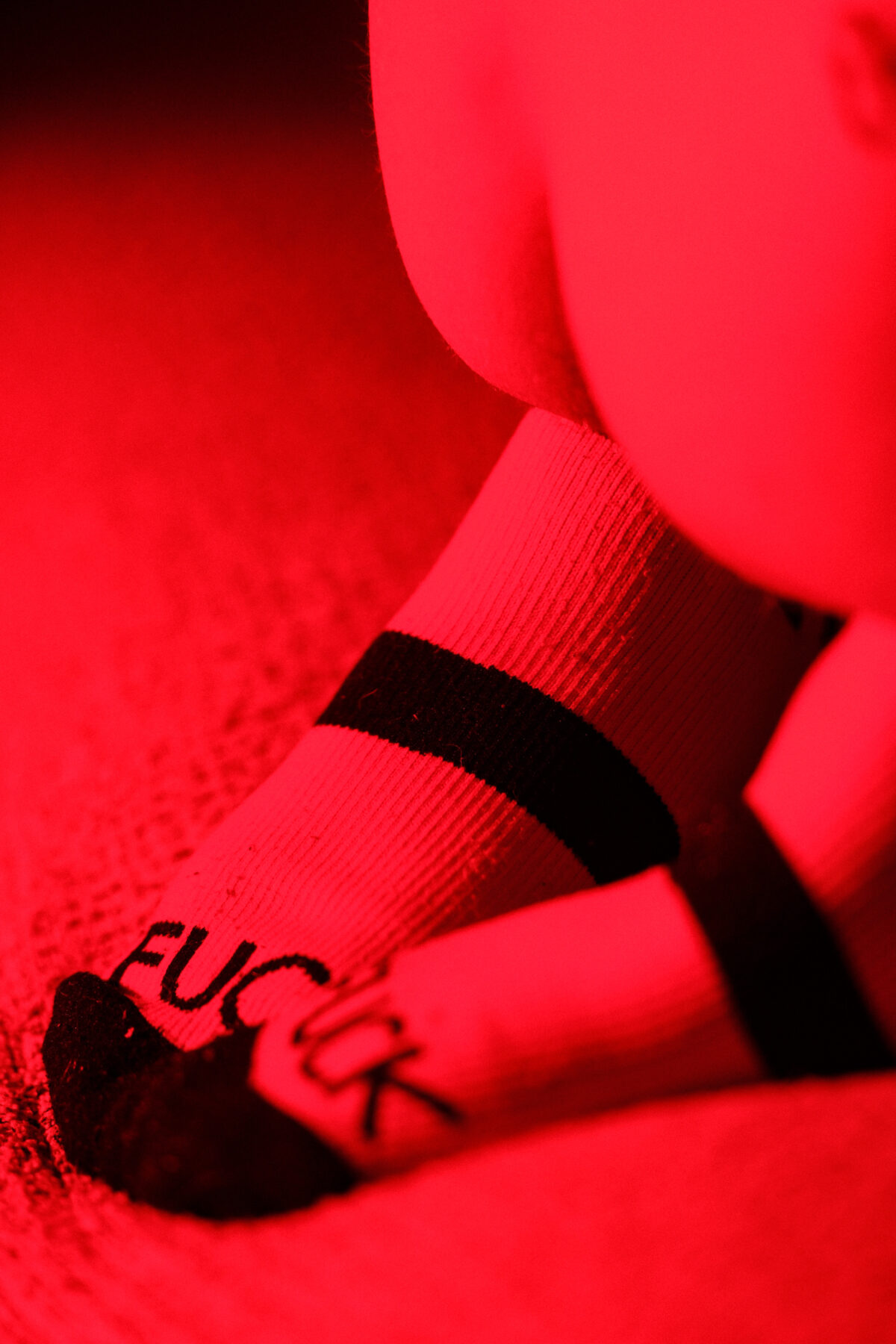 Gros plan rouge sur une chaussette floquée "FUCK" à bande noire, cheville et pied d'Angel Dust.