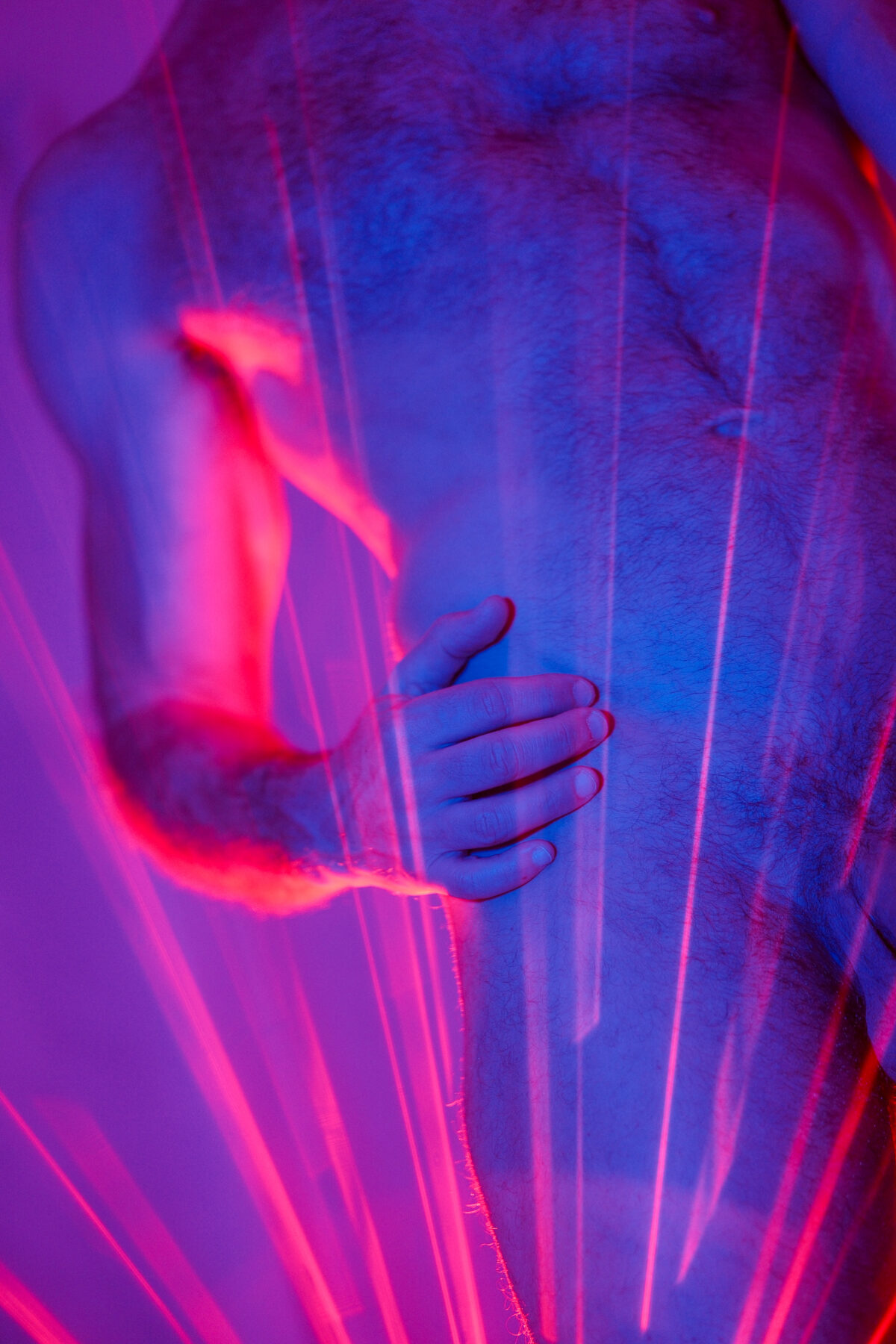 Gros plan sur un torse et une main traversés de faisceaux de lumière rouge et bleue, effet artistique