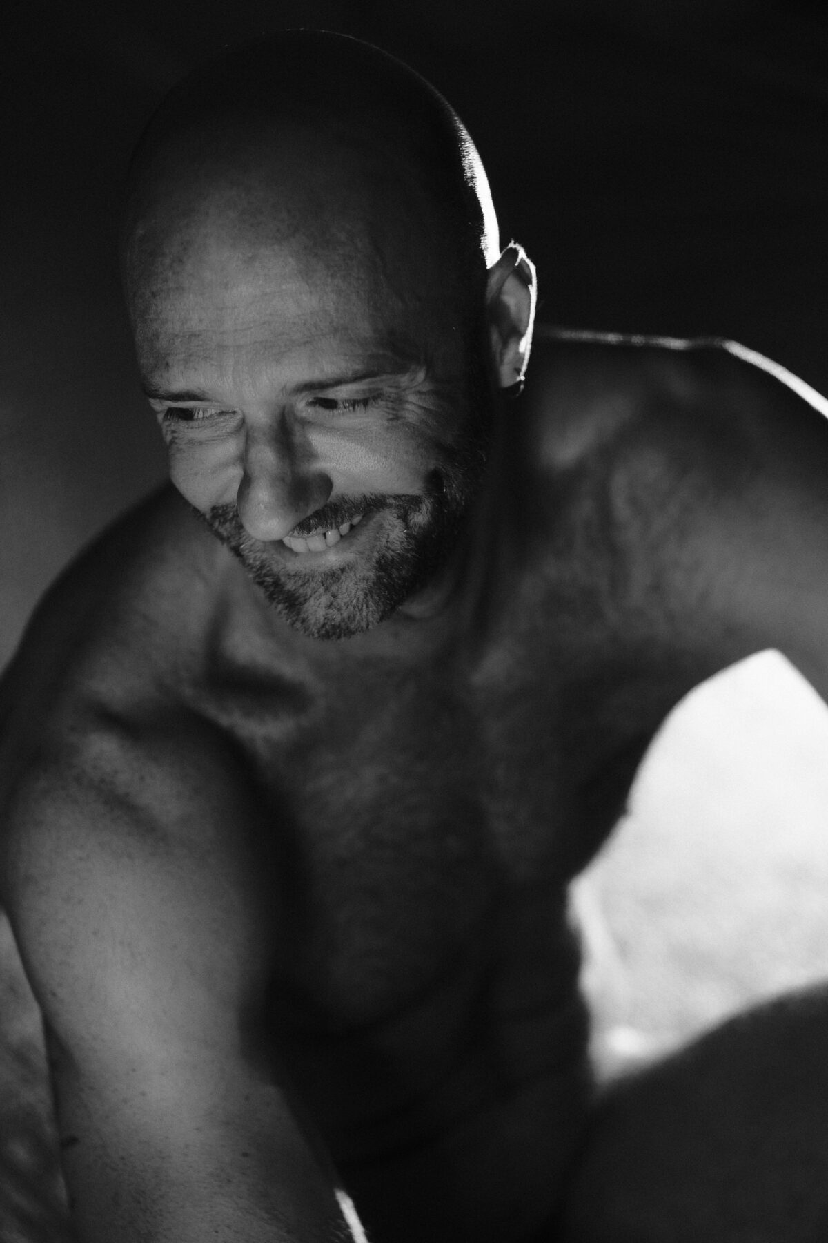 Portrait noir et blanc de Benoit souriant, regard baissé, lumière naturelle douce