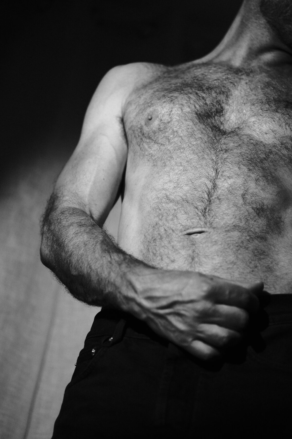 Gros plan noir et blanc sur le torse et le bras de Benoit, texture de peau et de pilosité, lumière douce
