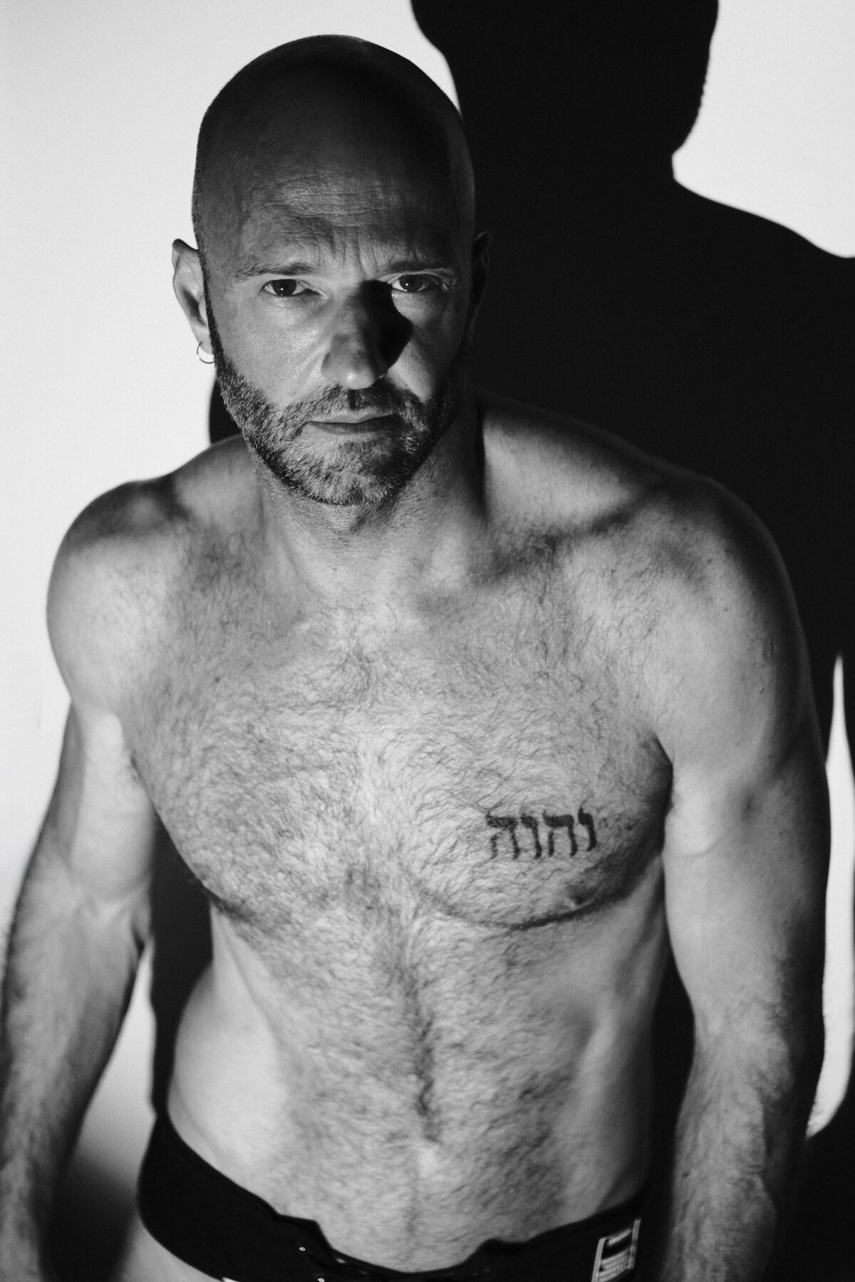 Portrait rapproché noir et blanc de Benoit, tatouage hébreu sur le torse, éclairage latéral contrasté