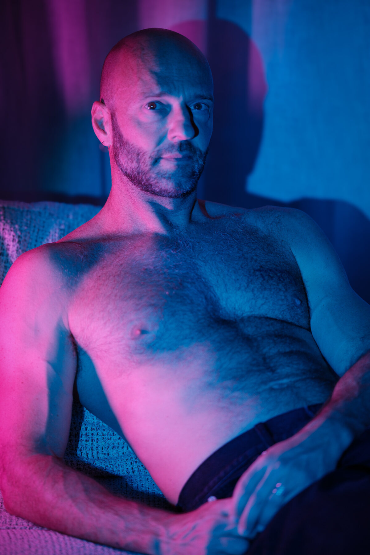 Portrait de Benoit assis, torse nu, regard vers l'objectif, éclairage gélatiné rose et bleu, ambiance intimiste