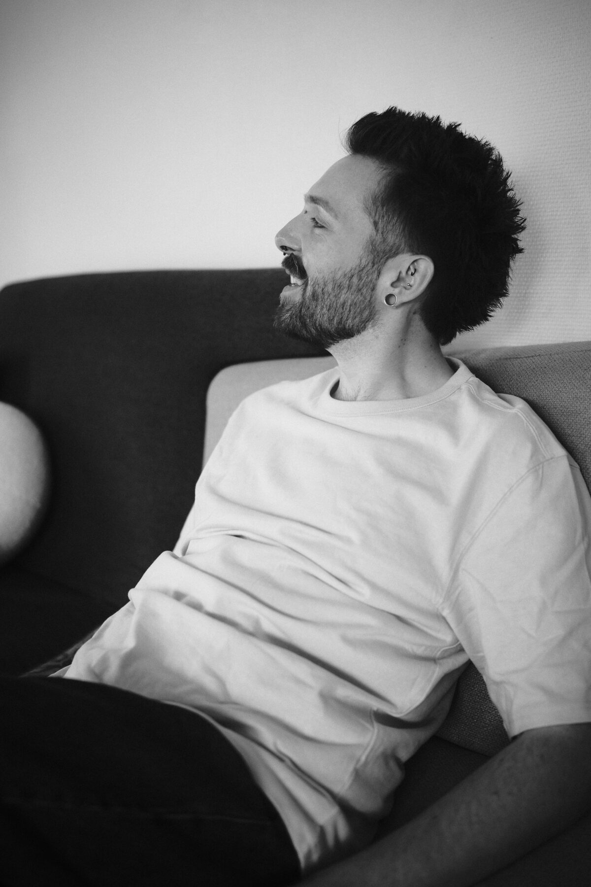 Portrait noir et blanc de François de profil, éclat de rire, piercings et plugs à l'oreille, tee-shirt blanc