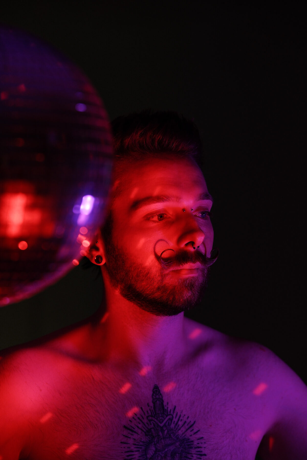 Portrait de François torse nu sous lumière rouge, boule à facettes, moustache en guidon, tatouage sur le torse