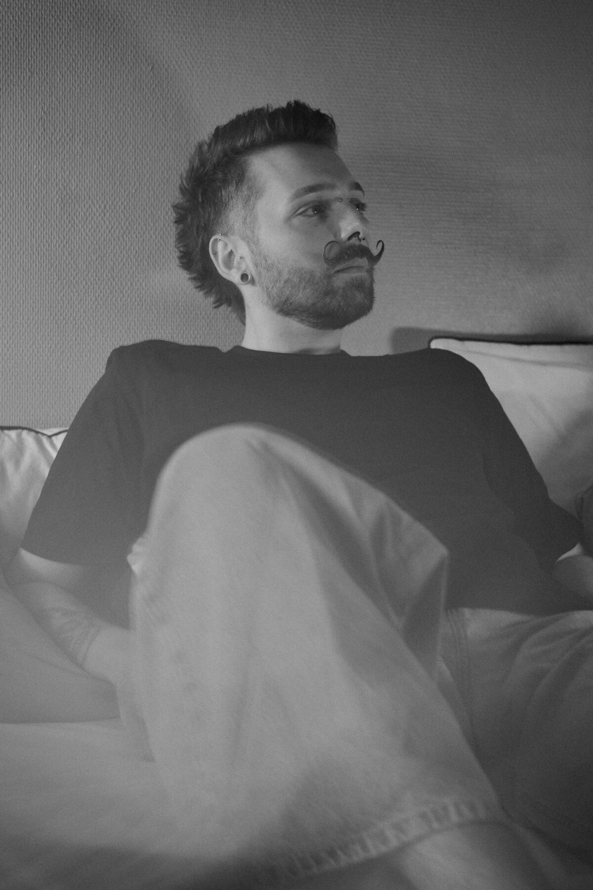 Portrait noir et blanc de François assis sur un lit, genou relevé, tee-shirt noir, regard de côté