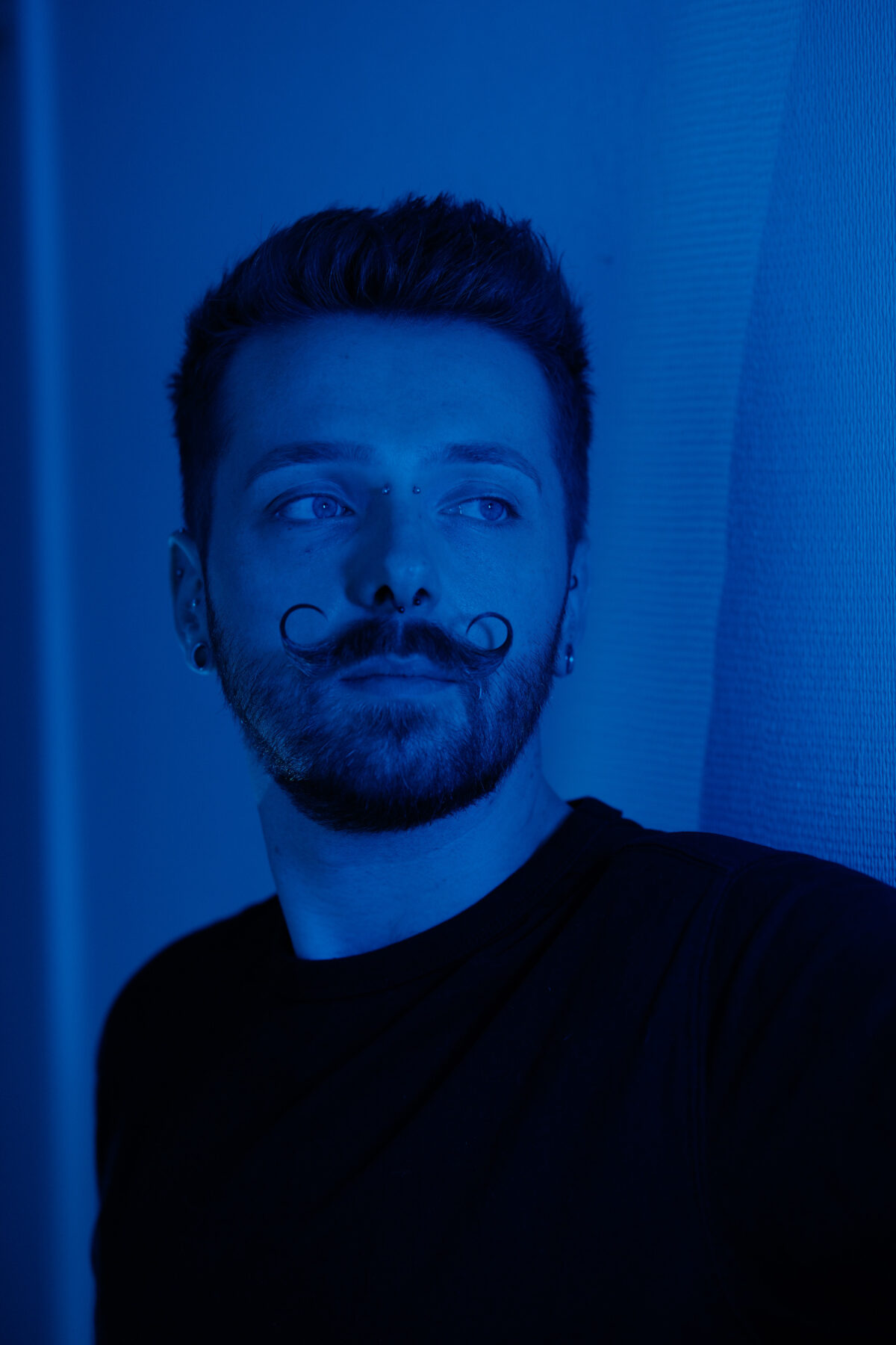 Profil de François sous une lumière bleue, piercings à l'oreille visibles de près.