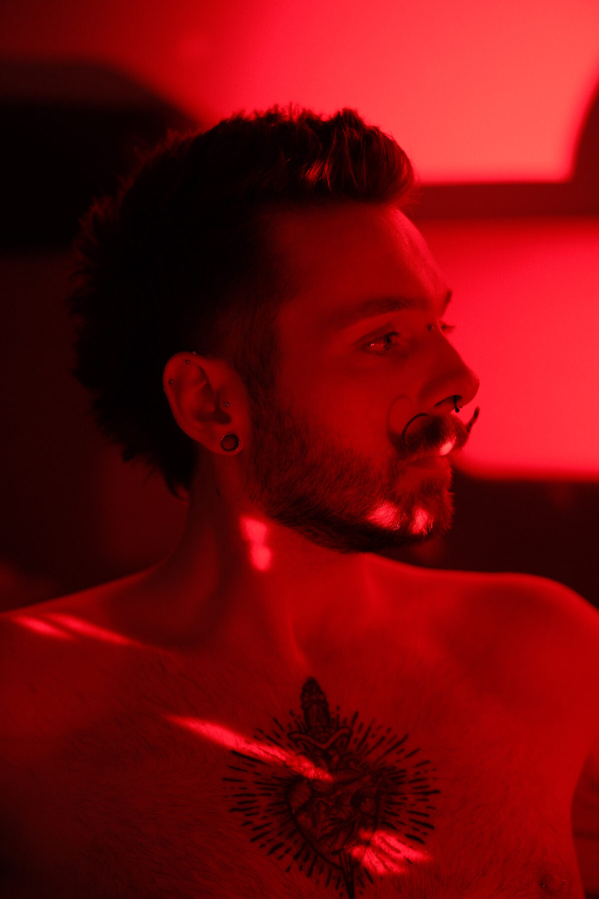 Profil de François torse nu sous une lumière rouge, plug à l'oreille visible.