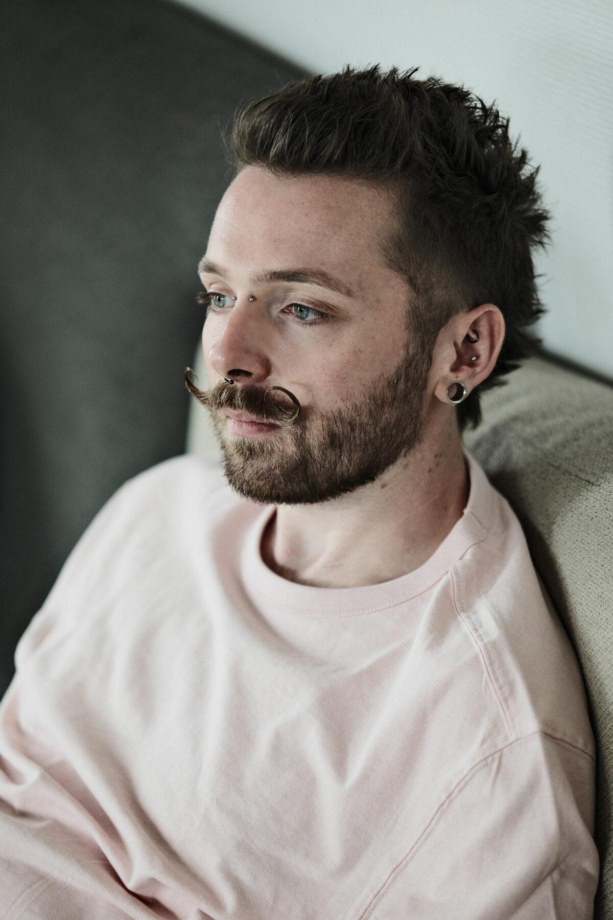 Portrait de François en tee-shirt rose pâle, regard de côté, moustache en guidon, plug à l'oreille