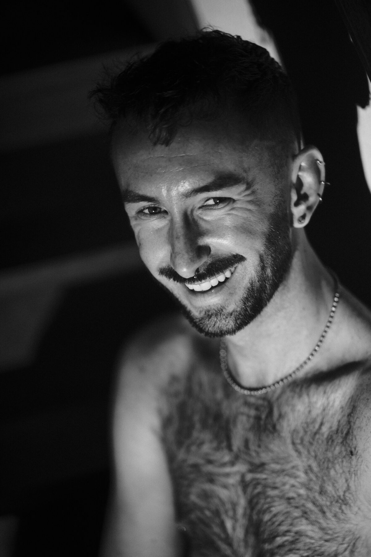 Portrait souriant de Hugo (de Lille) en noir et blanc, piercings à l'oreille, débardeur