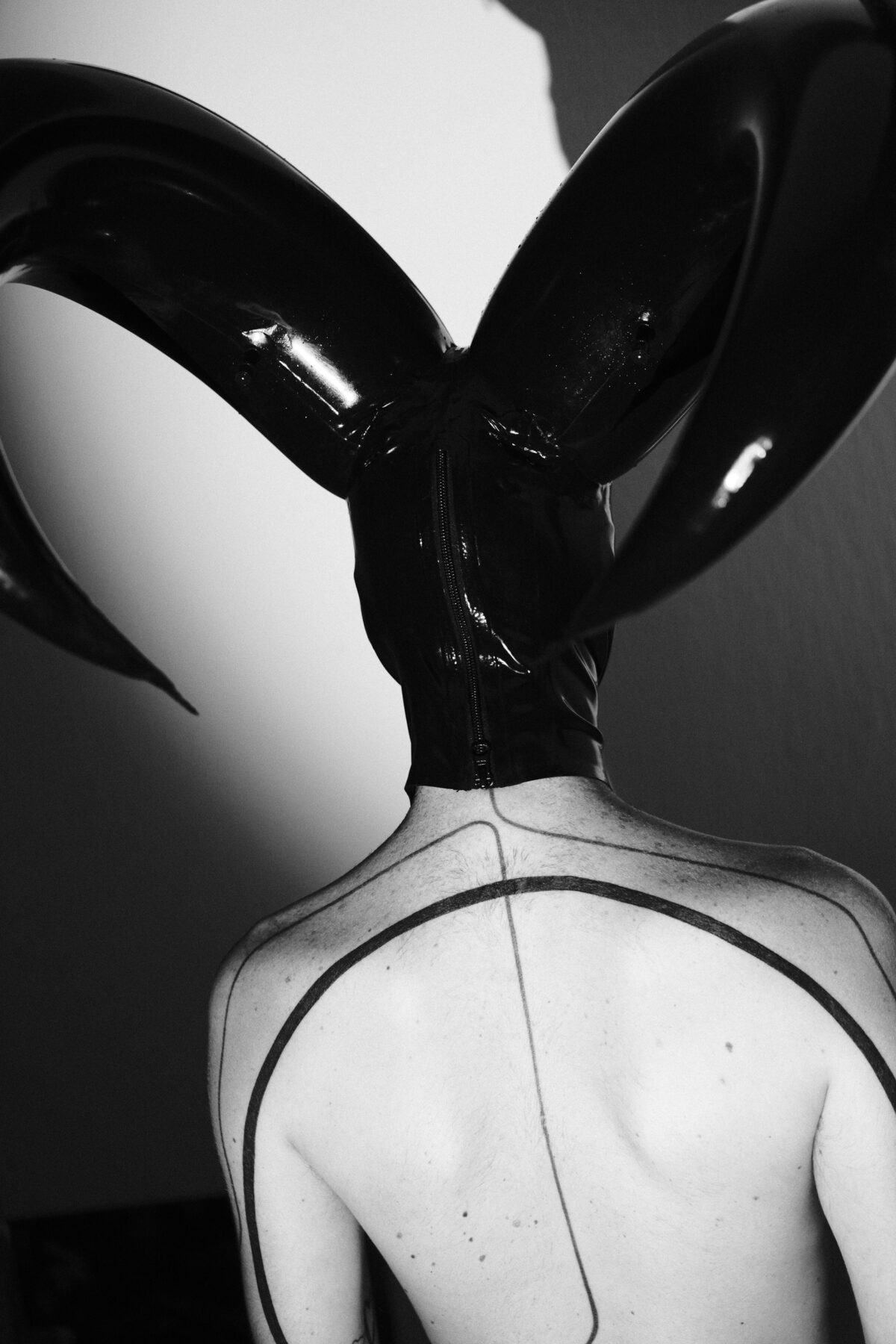 Portrait de dos de Hugo (de Lille) en noir et blanc, capuche en latex à cornes, dessin graphique tracé sur le dos