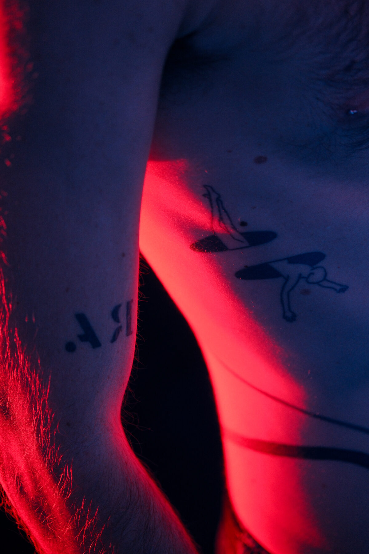 Gros plan sur le bras et le torse de Hugo (de Lille), tatouages, éclairage rouge
